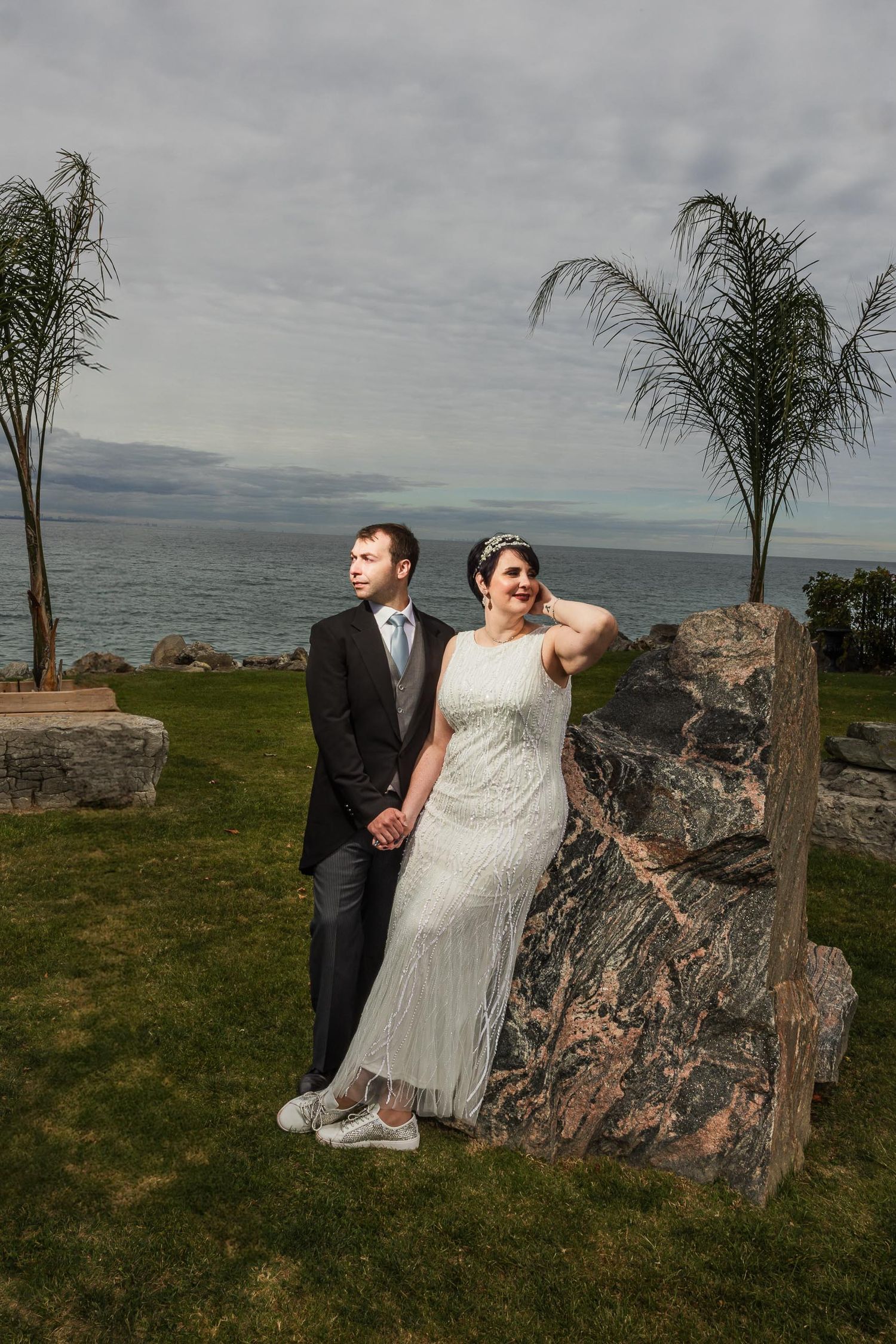 Seaside wedding portrait with couple posing against rocky coastal landscape.