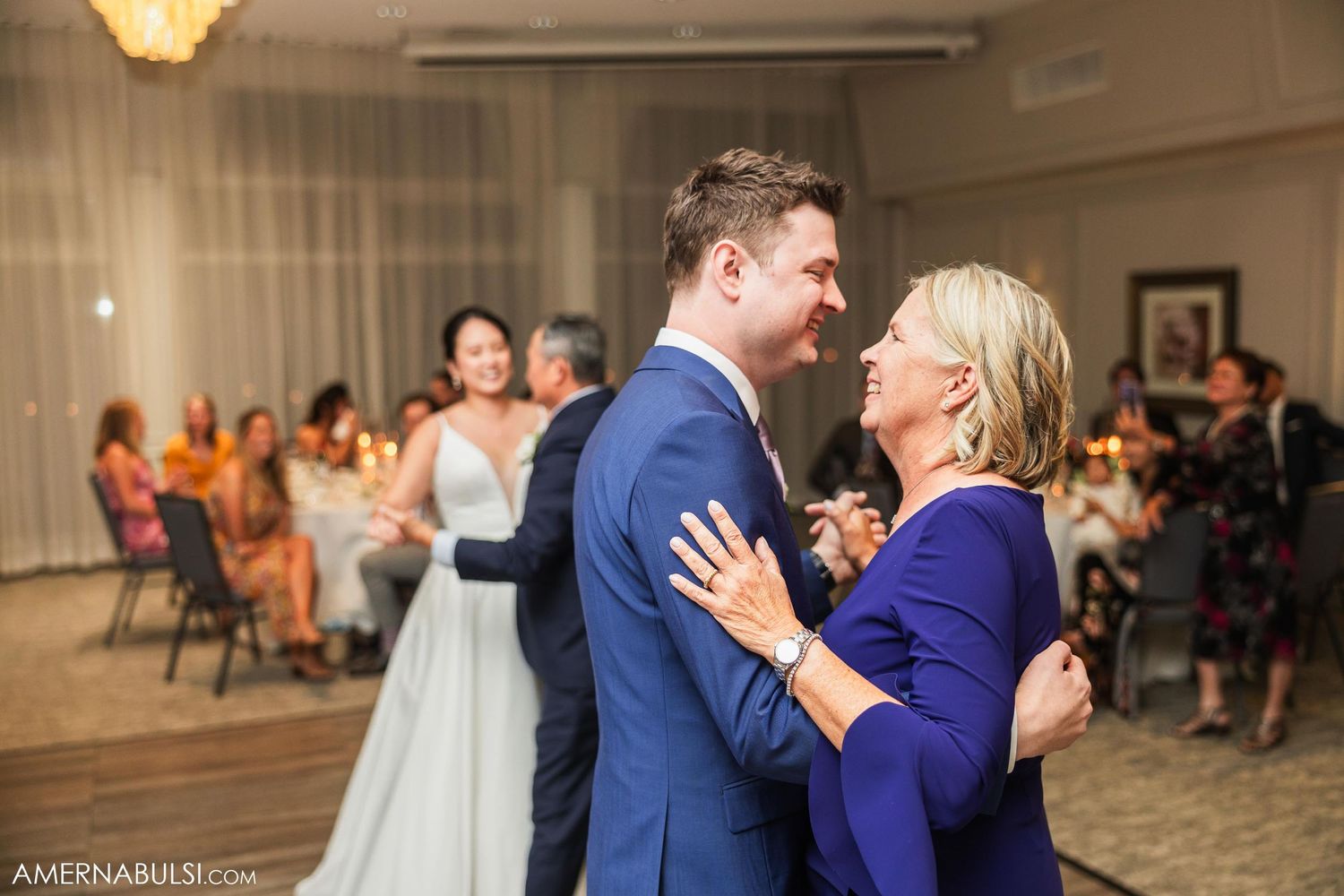 Tender moment shared between dancers at wedding reception with background guests.