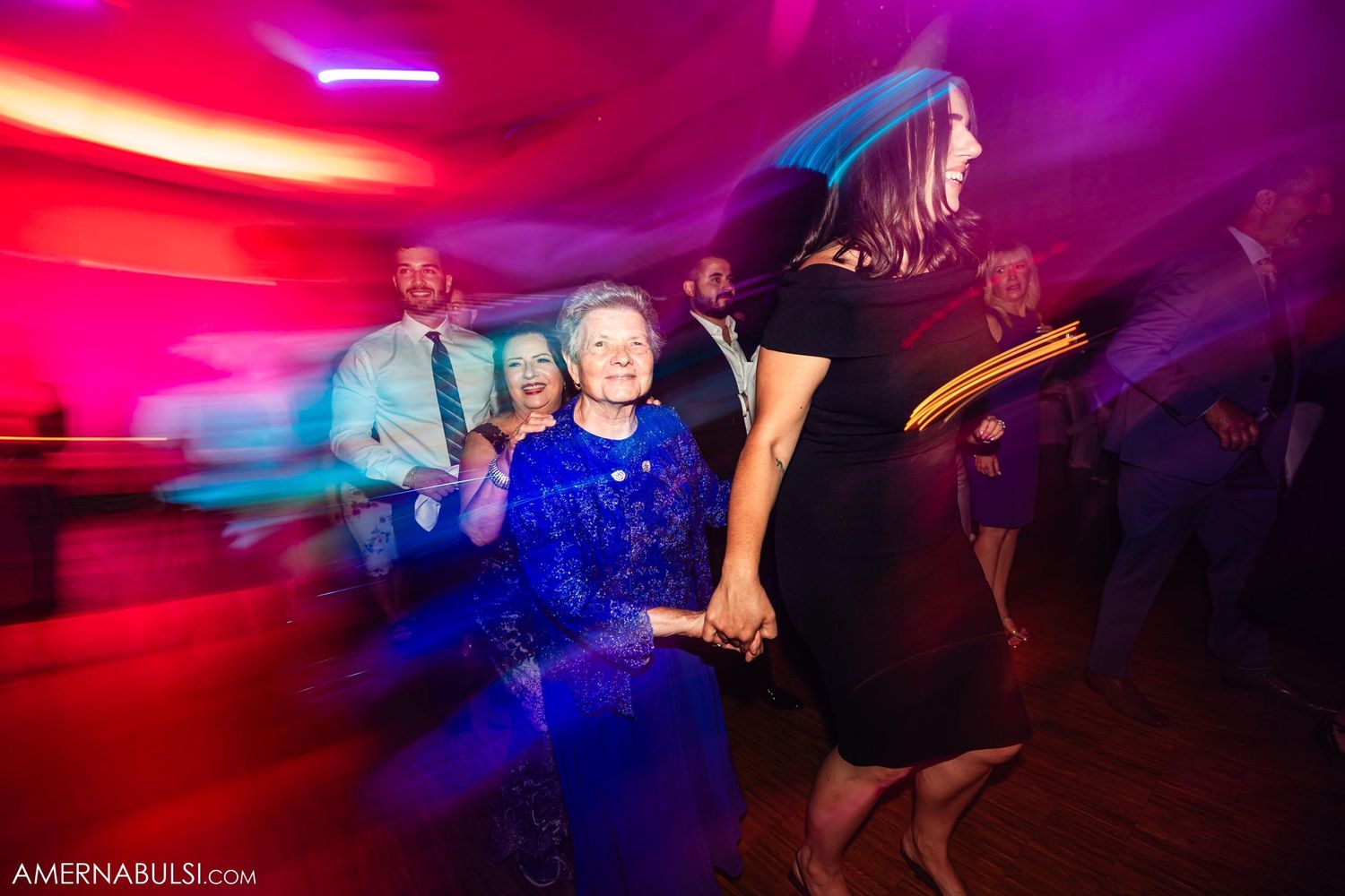 Wedding guests dancing under vibrant red and purple lighting effects on a dance floor.