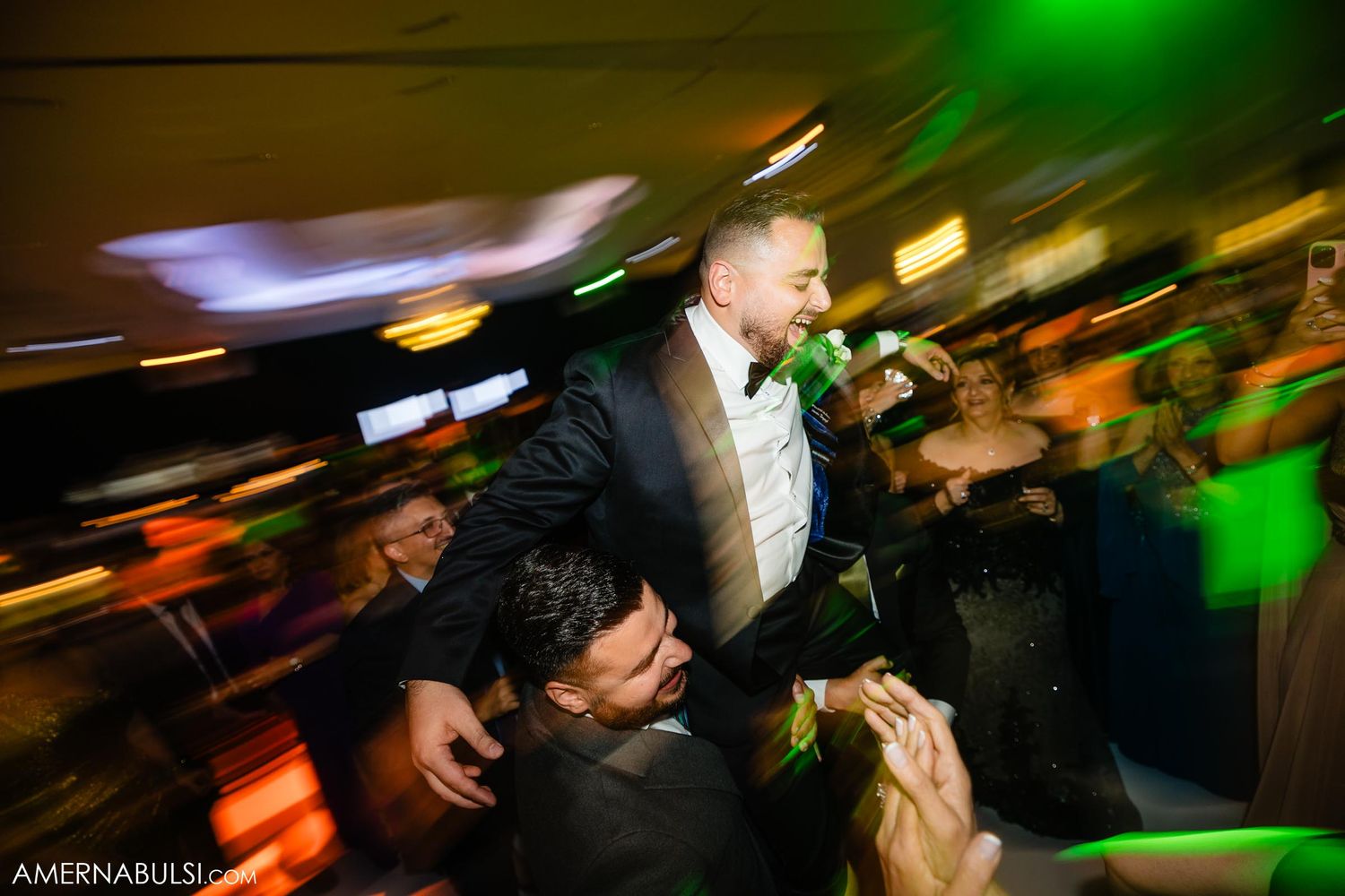 Dynamic party scene shows celebratory dancing with green lighting effects at a wedding reception.