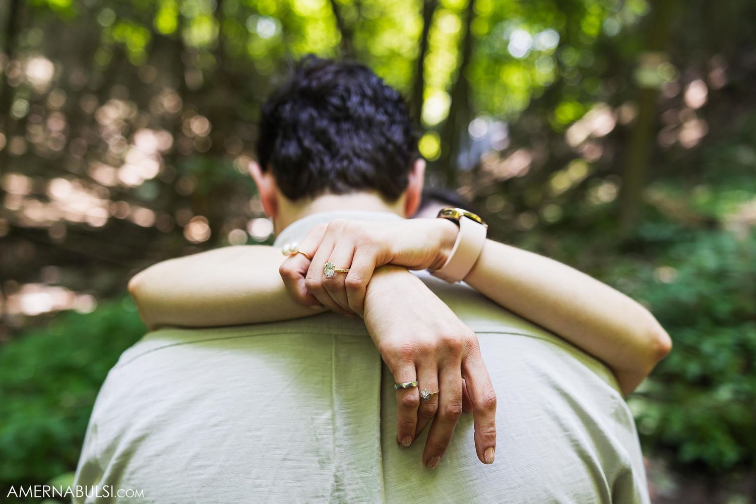 Close-up of hands embracing from behind showing wedding ring detail.