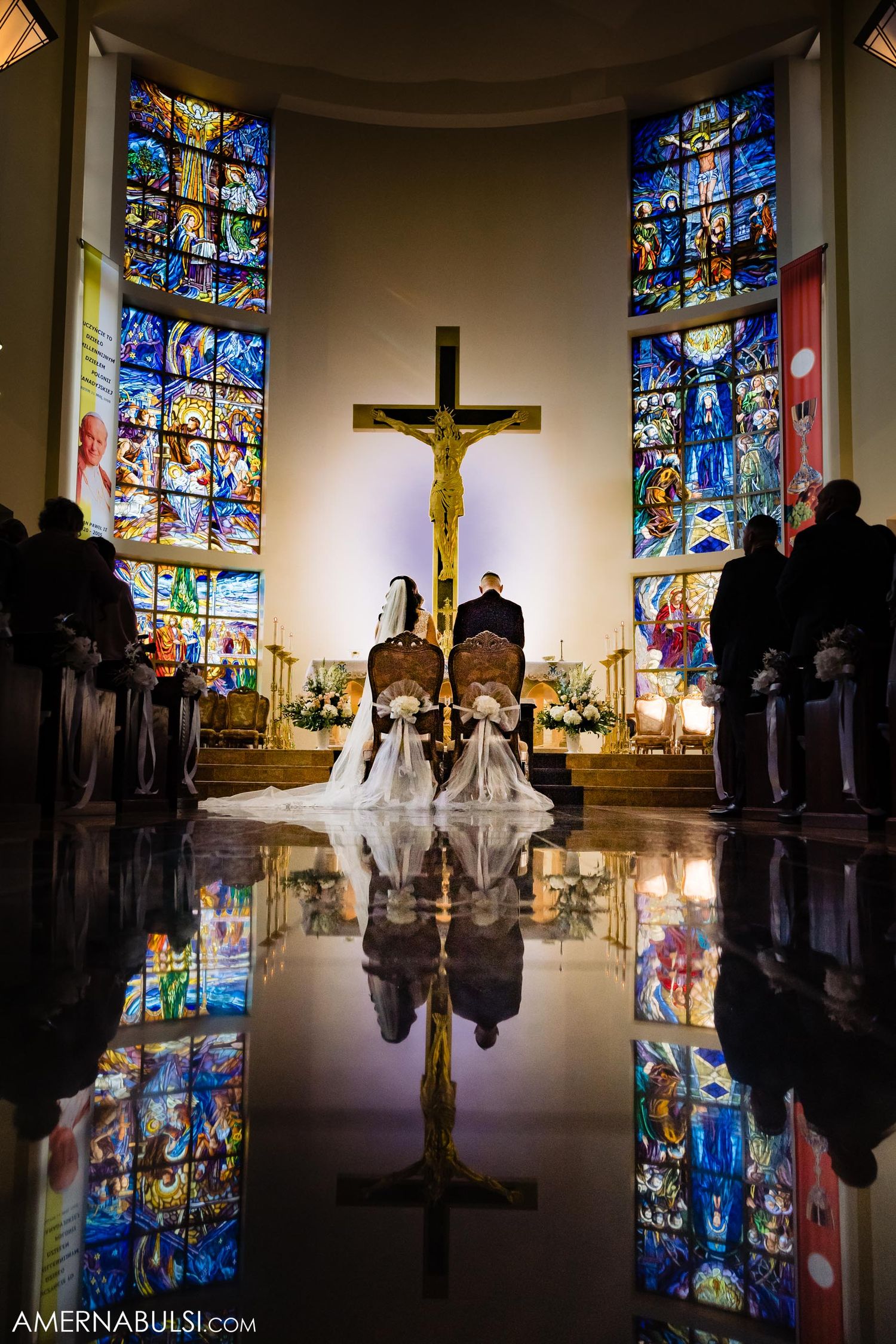 Dramatic church wedding photo with couple reflected in polished floor beneath stained glass windows.