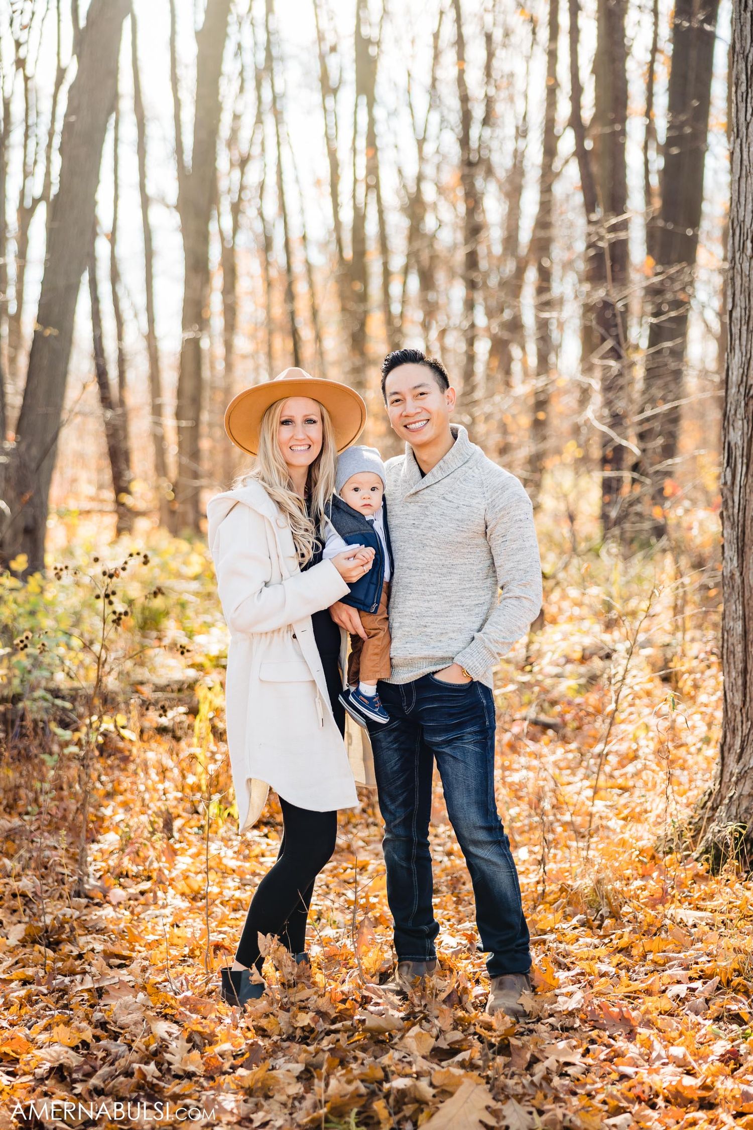 Family portrait in autumn woods with person wearing tan hat and white cardigan.