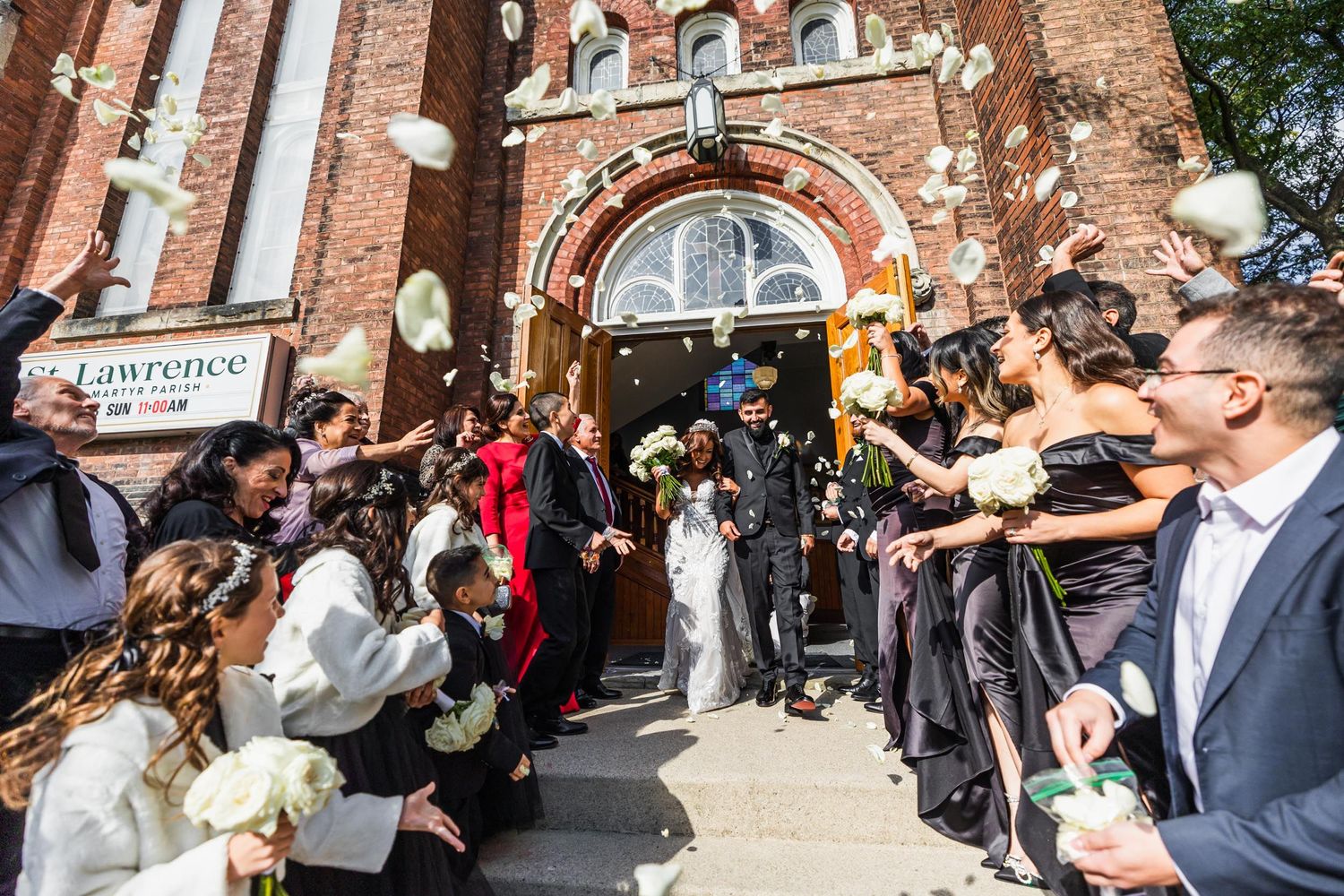 Church wedding exit celebration with guests throwing petals outside ornate brick facade.
