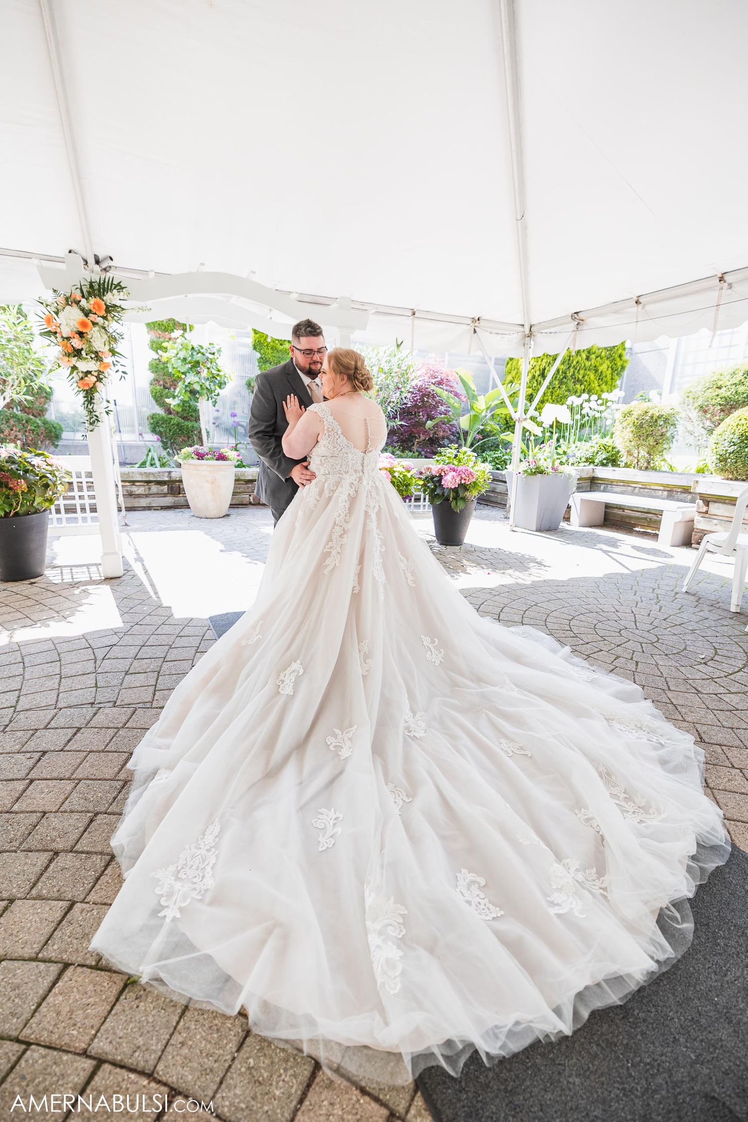 A couple sharing their first dance under a white tent with flowing wedding gown train.