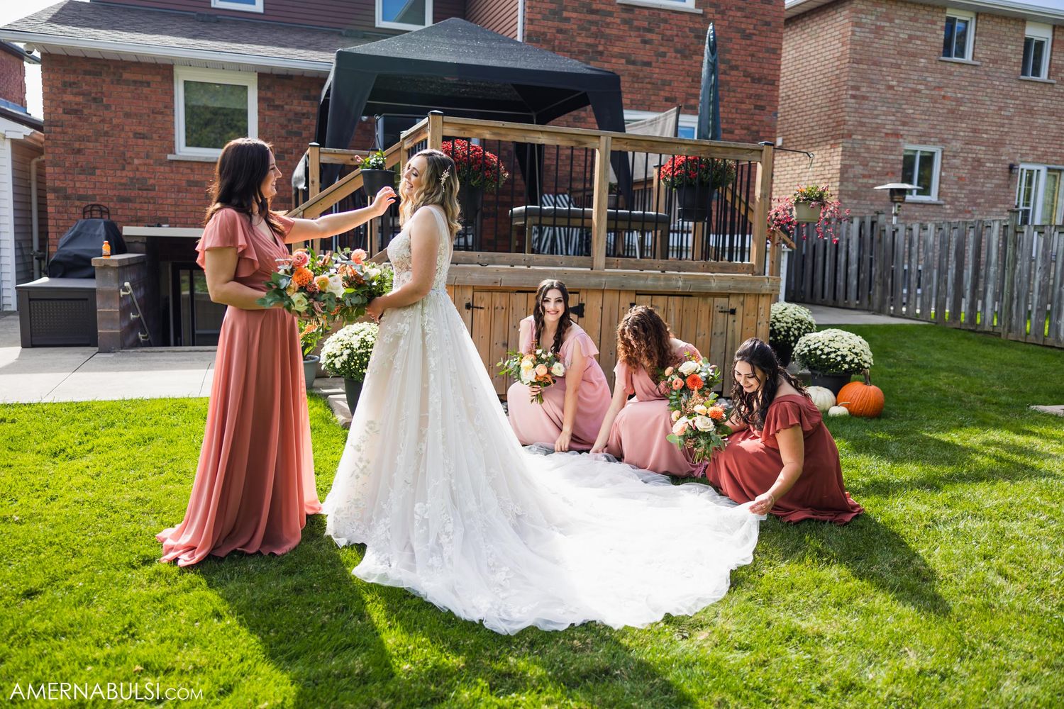 Wedding party arranged on lawn helps arrange bride's dress train during photo session.
