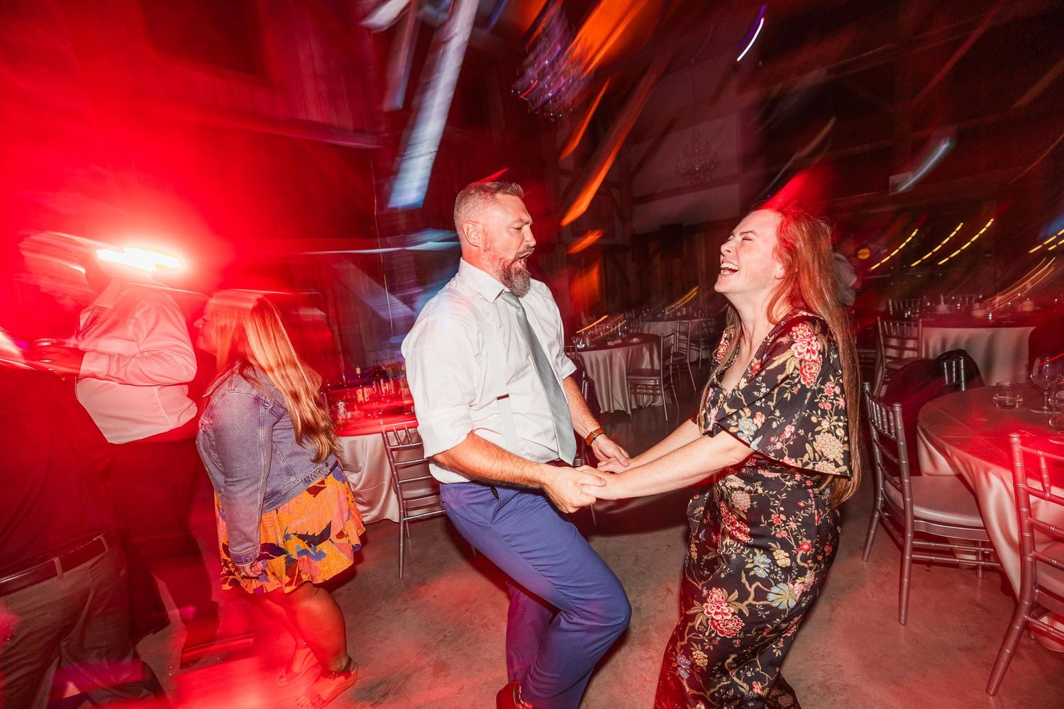 Wedding guests dancing under red lighting at reception party.