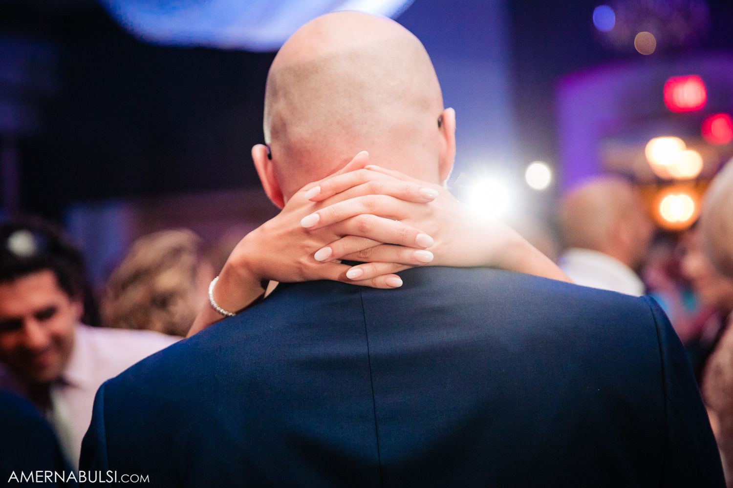 A tender moment captured from behind as guests dance at an evening reception.