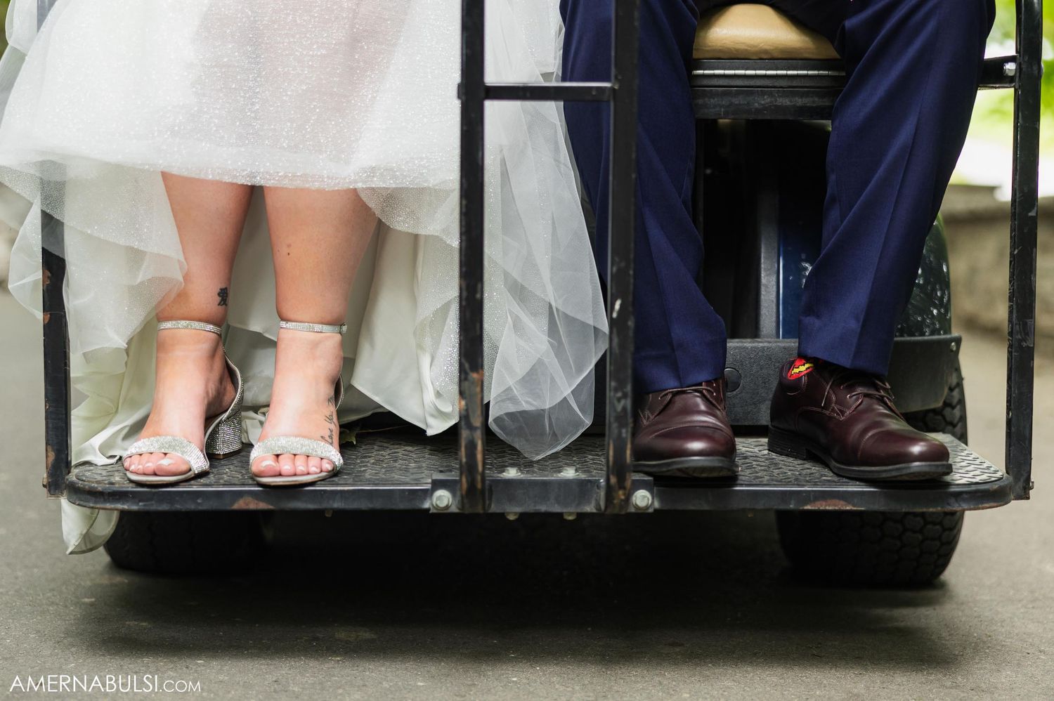 Wedding shoes detail shot showing bride's sparkly heels and groom's brown dress shoes on a black platform.