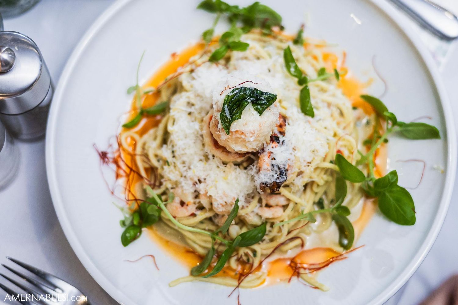 Pasta dish with shaved parmesan, microgreens and sauce served on white plate.