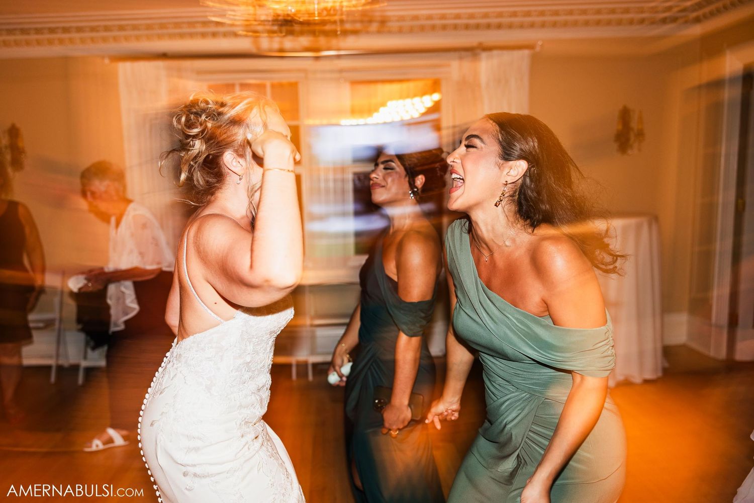 Wedding guests dancing and celebrating in elegant ballroom with chandelier.