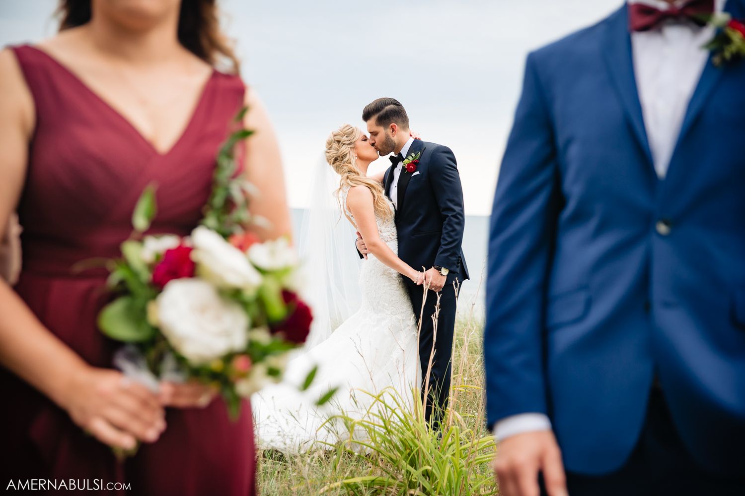 Wedding party members in navy suits and burgundy dresses pose together outdoors.