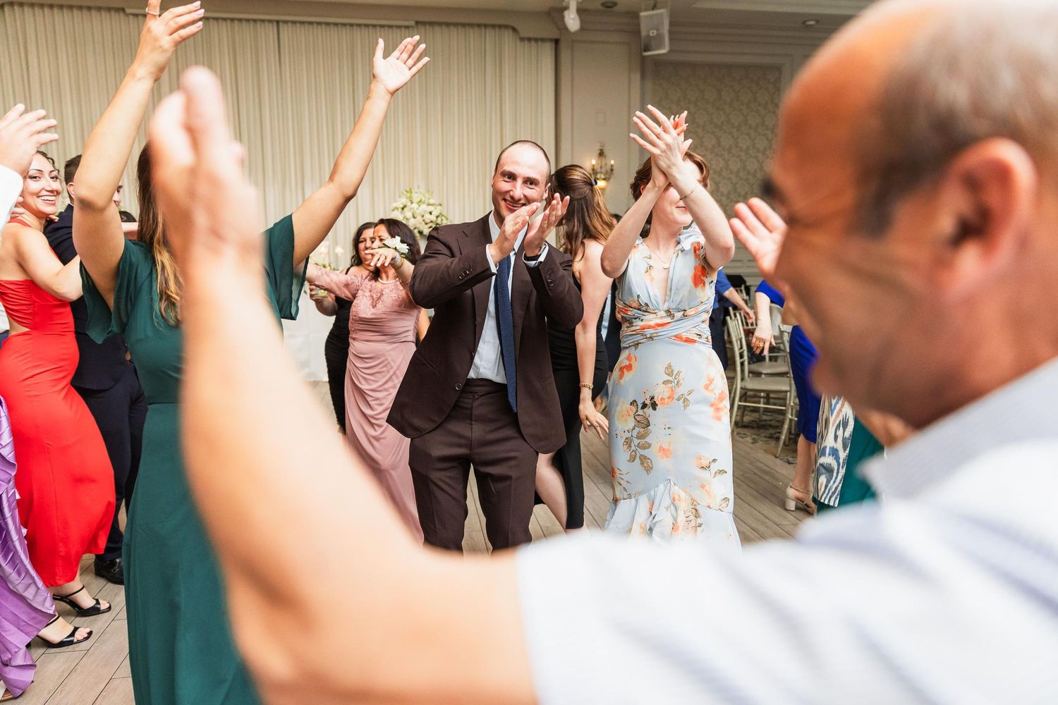 Wedding guests dance and celebrate with raised hands during a lively reception party.