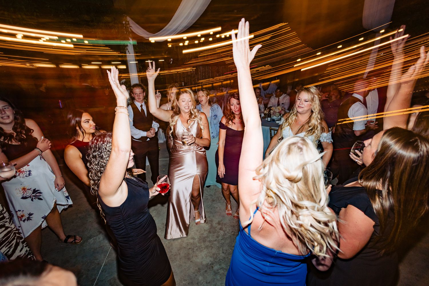 Wedding party guests dancing enthusiastically on a crowded dance floor under warm lighting.