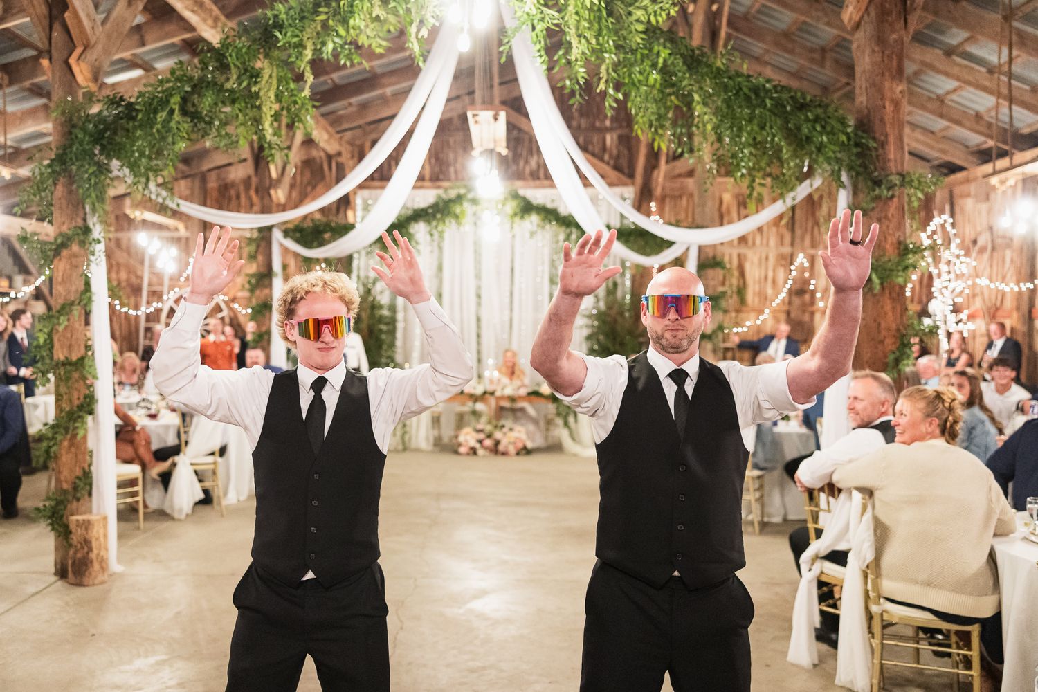 Wedding couple embraces while dancing in a rustic barn venue decorated with flowing white fabric and greenery.