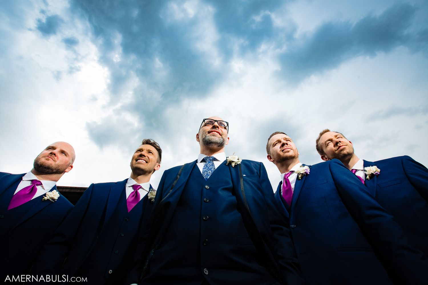 Dramatic low angle shot of wedding party members against a moody blue sky.