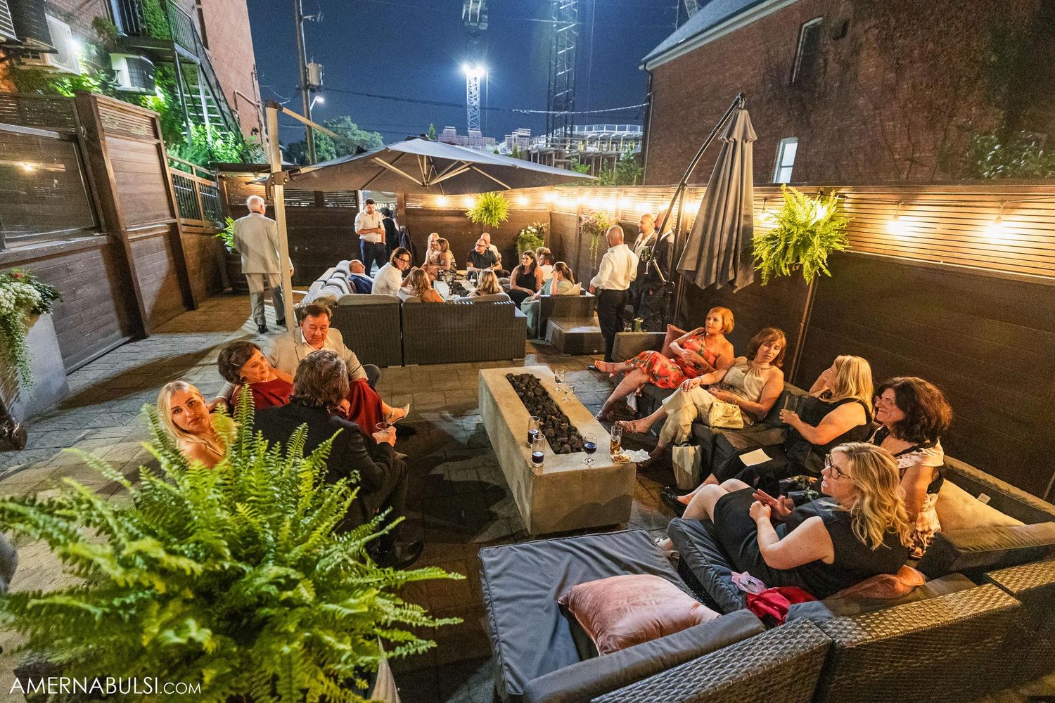 Outdoor rooftop lounge area with guests relaxing on cushioned seating under night sky.