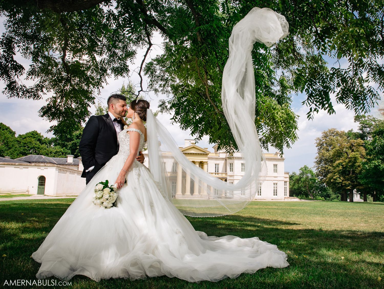 Romantic wedding portraits captured in front of a grand white mansion with lush greenery.