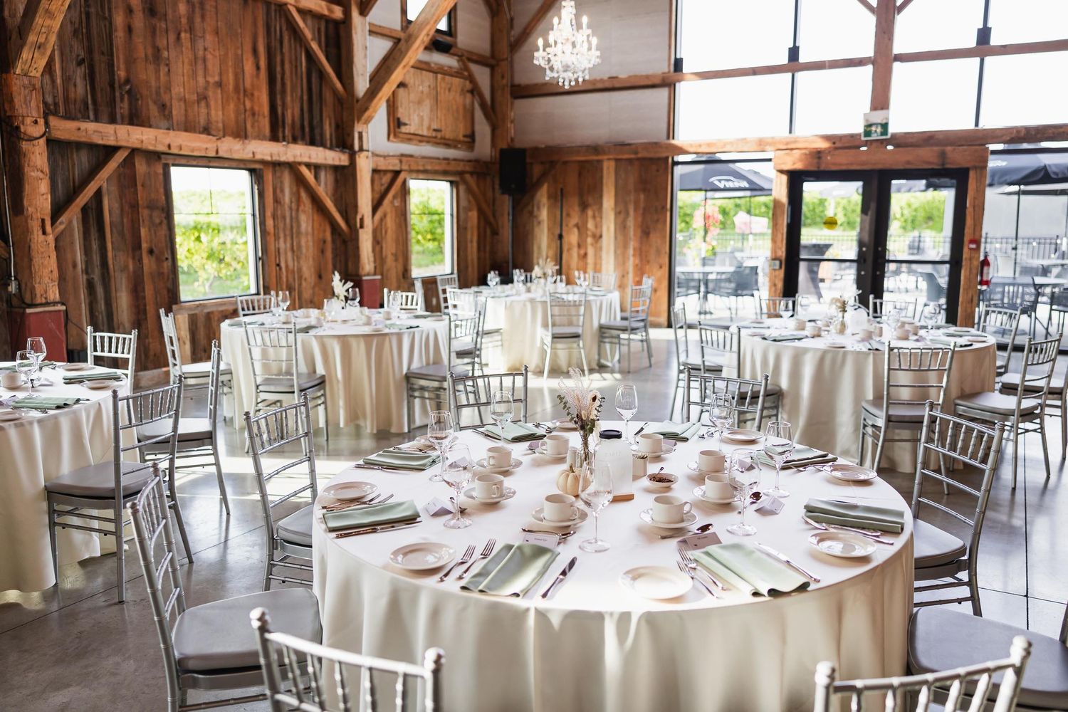 Elegant barn wedding venue with round tables, white linens, and silver chairs set for reception.