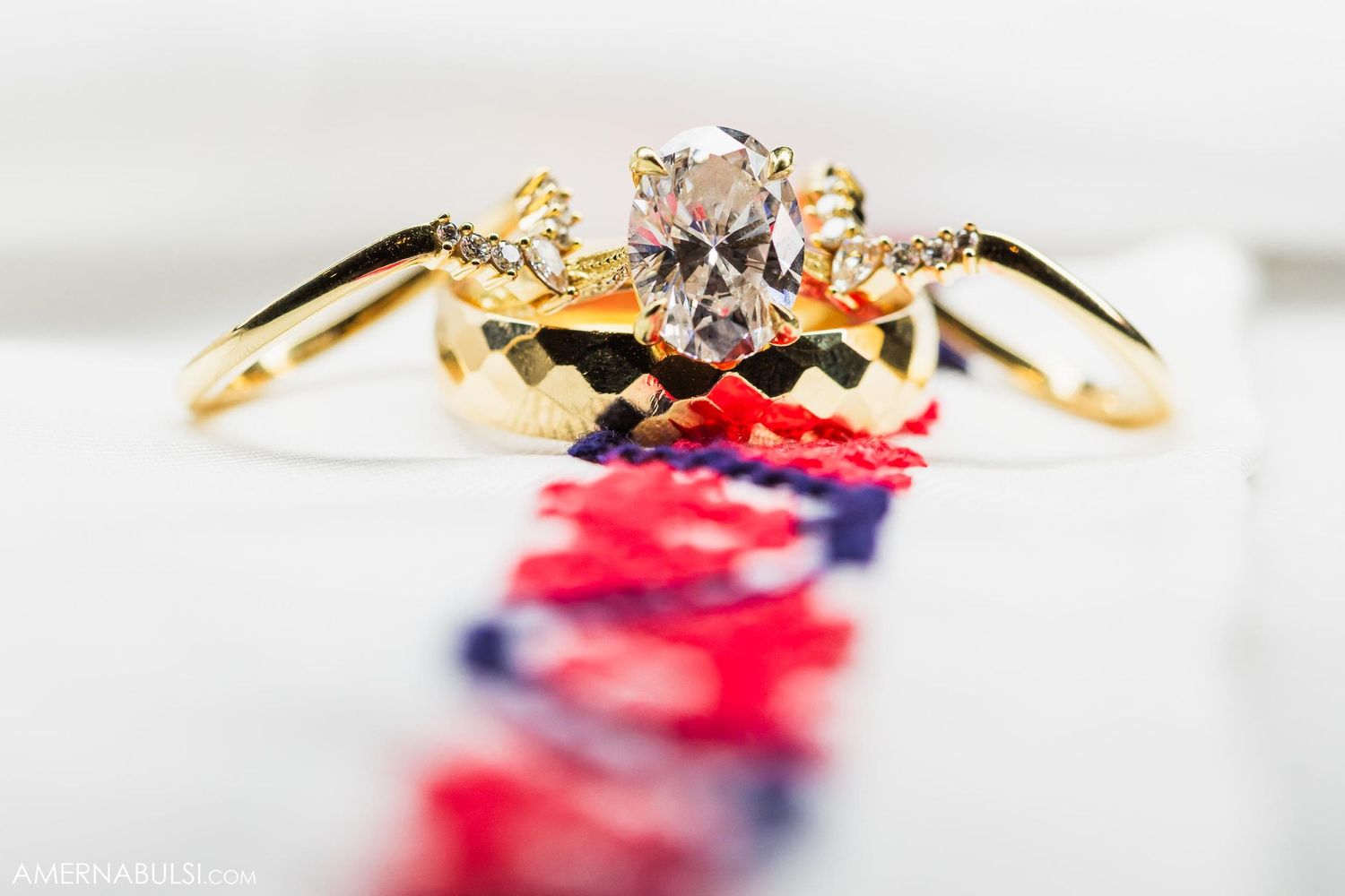 Gold engagement ring with diamond center stone displayed on red and blue pattern background.