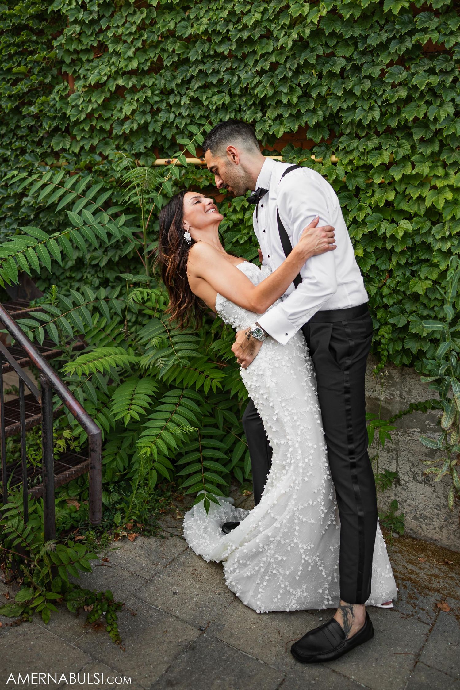 Wedding couple shares romantic moment against ivy-covered wall with ferns.