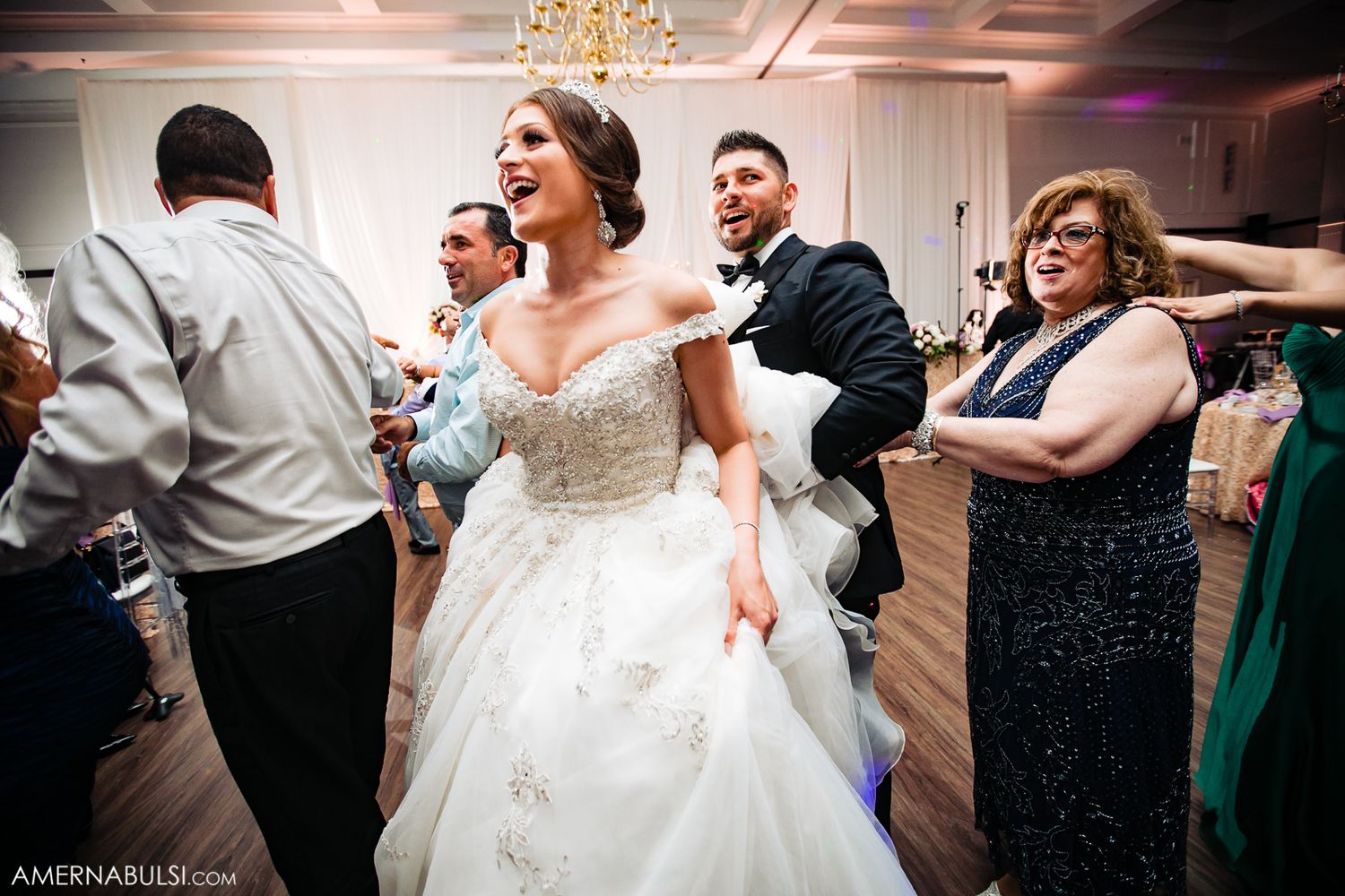 Wedding reception guests dancing and celebrating on a dance floor under elegant chandeliers.