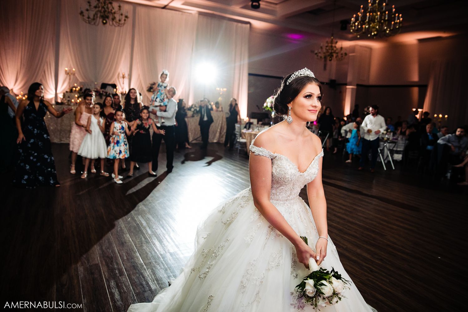 A beautiful ballroom wedding reception features a couple dancing together under warm chandelier lighting.