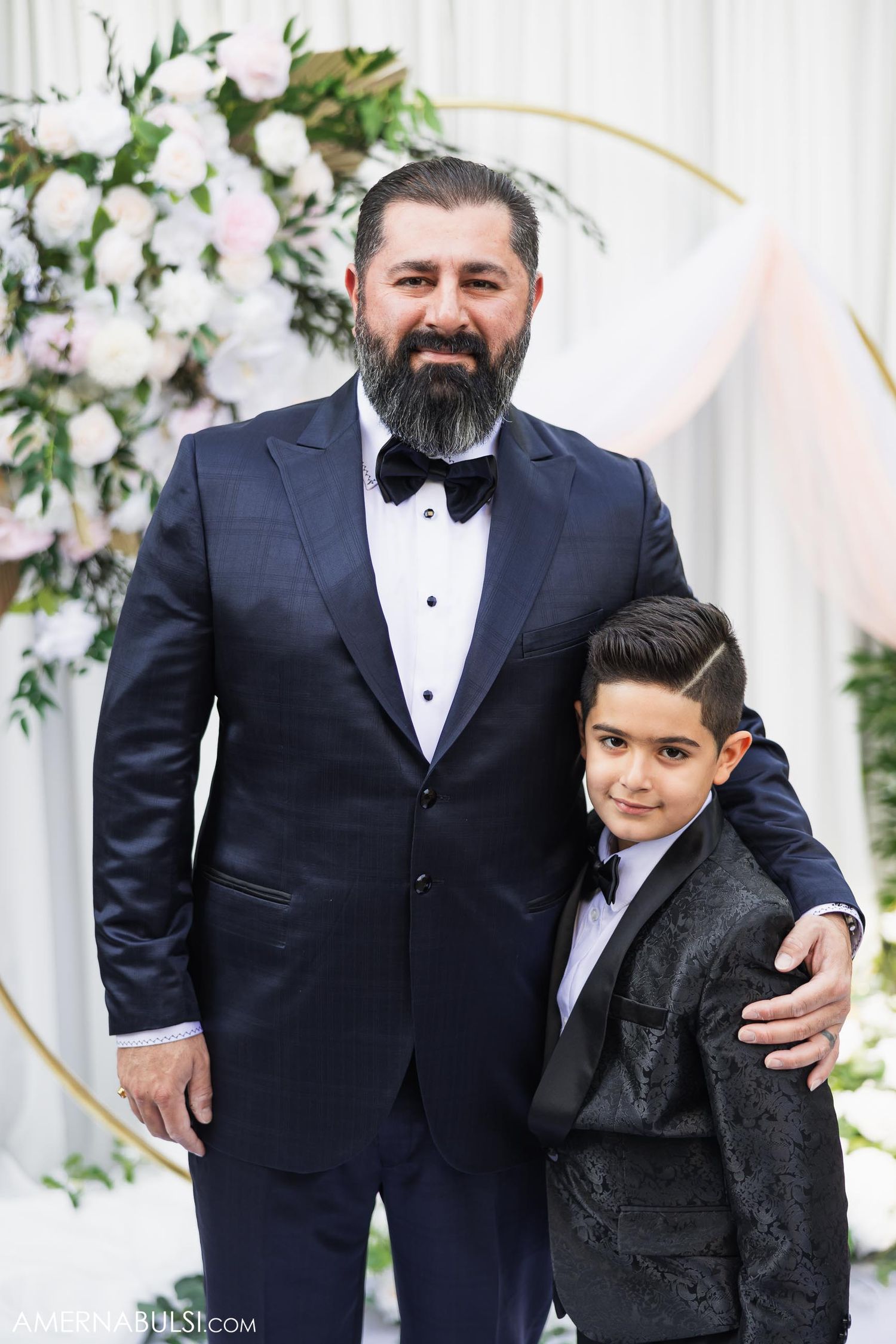 Formal portrait against floral wedding arch with white roses and greenery.