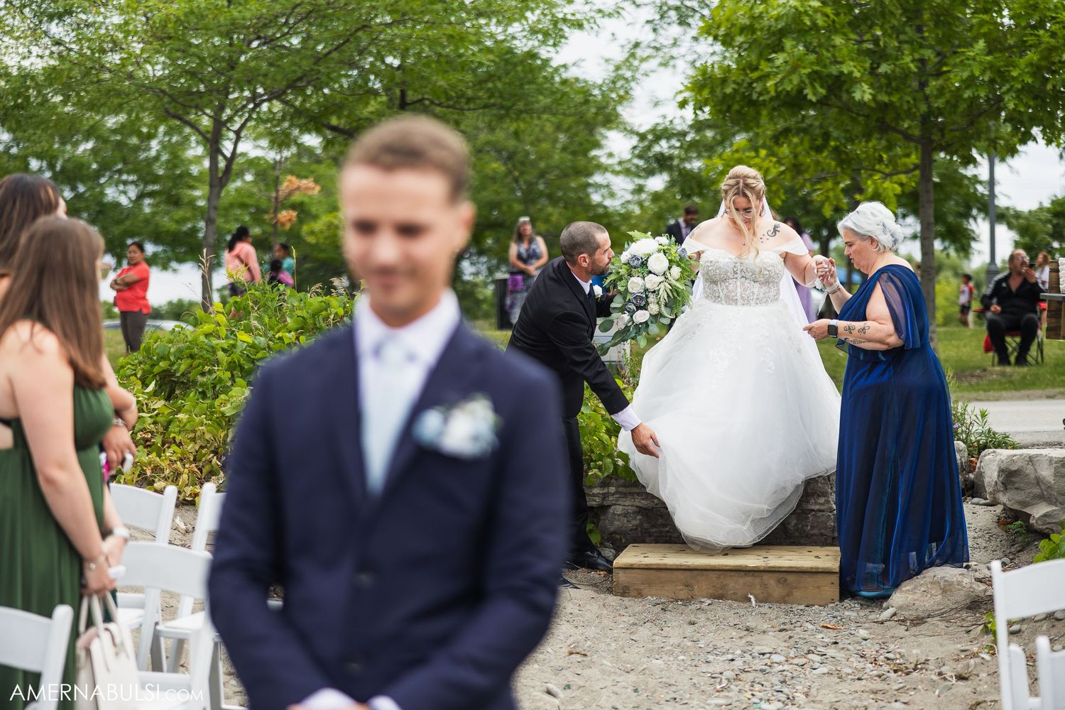 Guests in navy blue and formal attire gather outdoors at an elegant garden wedding ceremony.