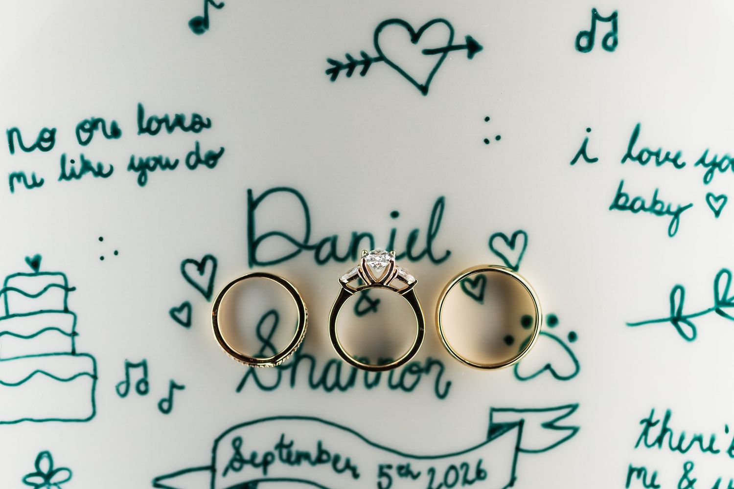 Wedding rings displayed on illustrated plate with Daniel and Sharon September 5th 2026 design.