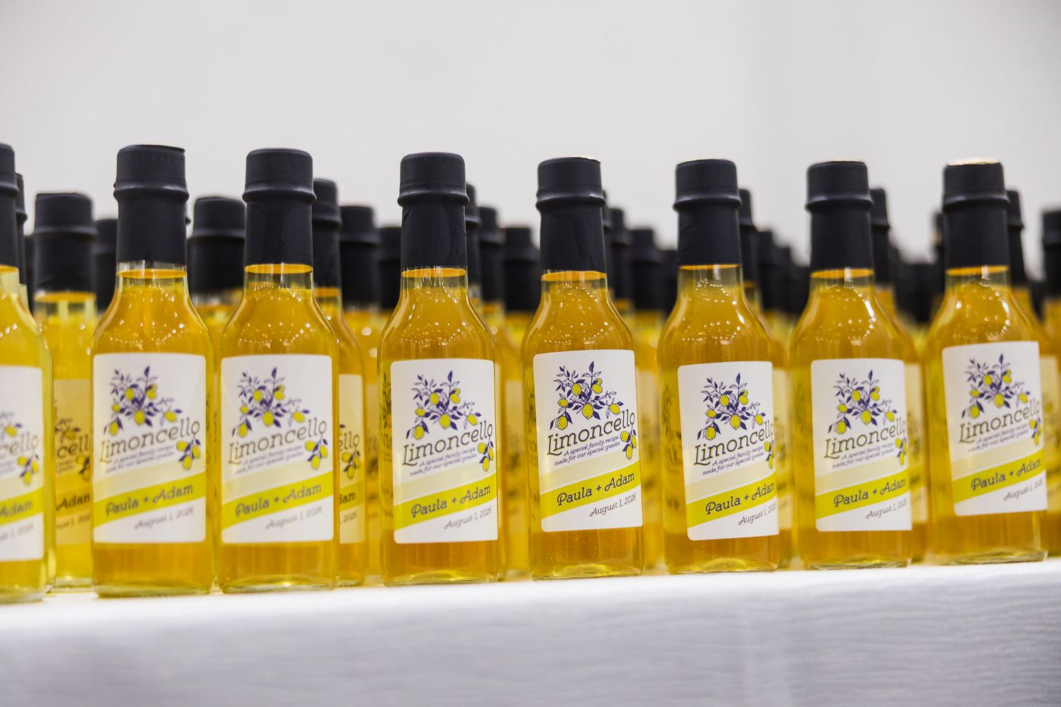 Rows of yellow oil bottles with floral labels displayed as wedding favors on a white table.