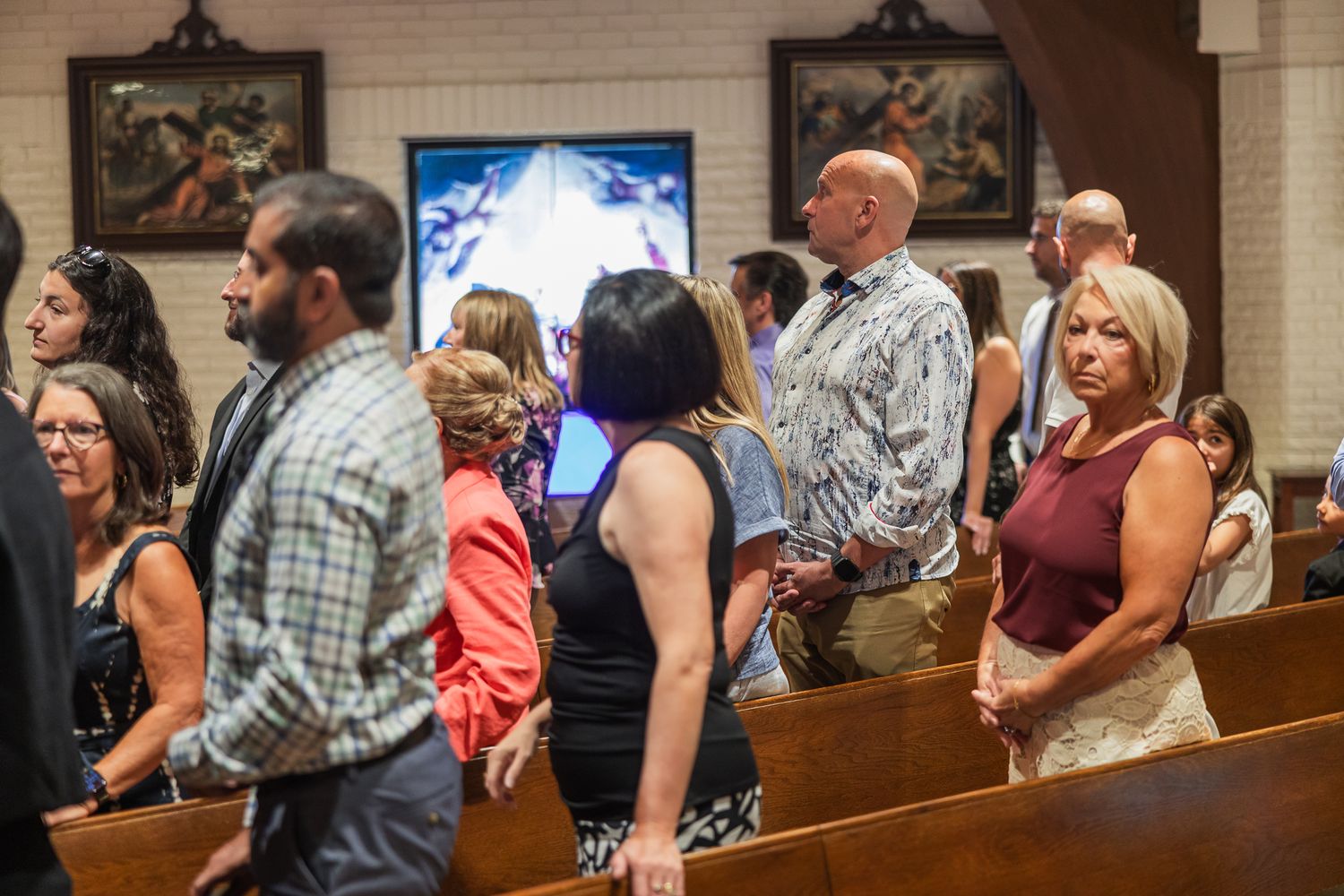 Wedding guests stand in church pews during a ceremony, dressed in colorful attire.