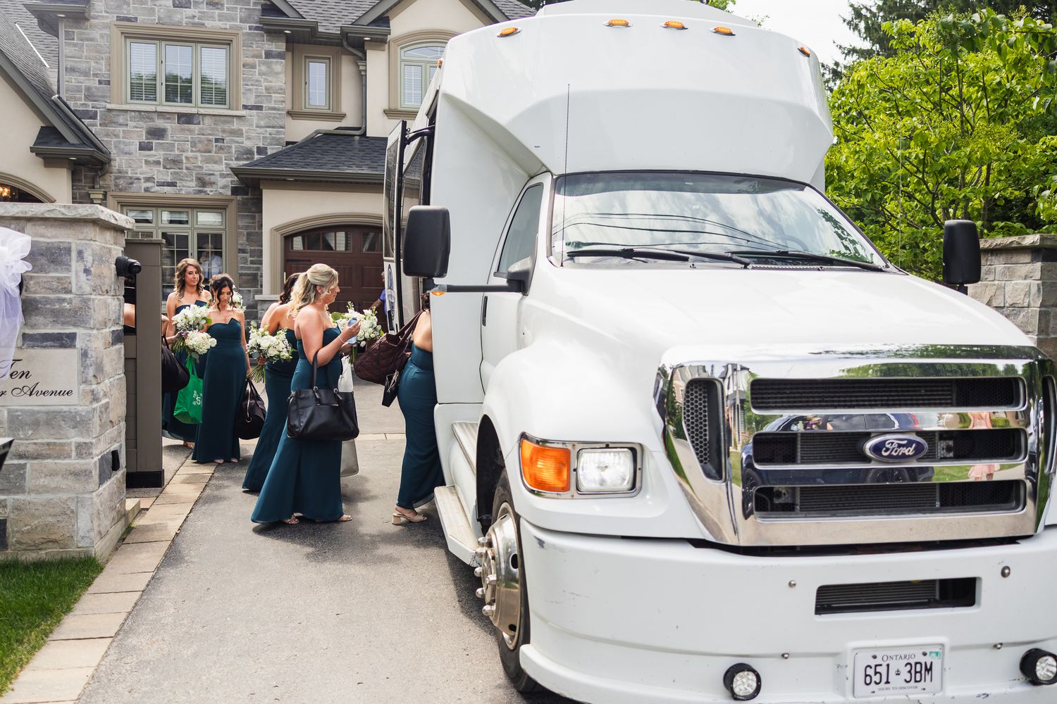 Bridesmaids in teal dresses boarding white Ford wedding party bus.
