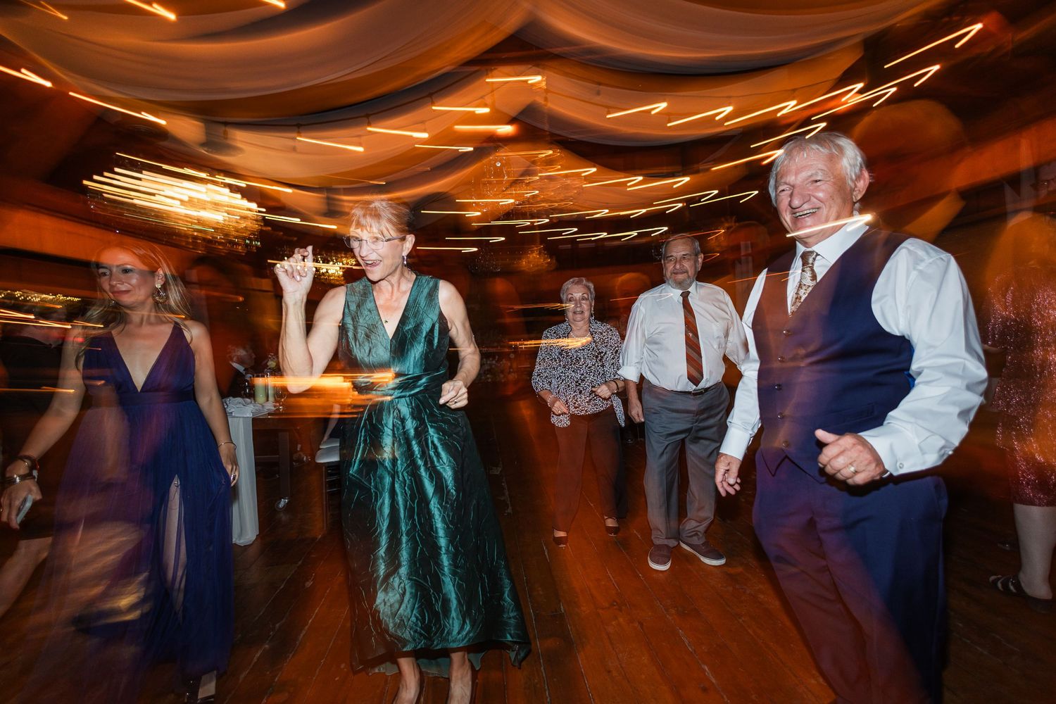 Guests dancing joyfully at a wedding reception, featuring elegant attire and warm, glowing lights on the dance floor.