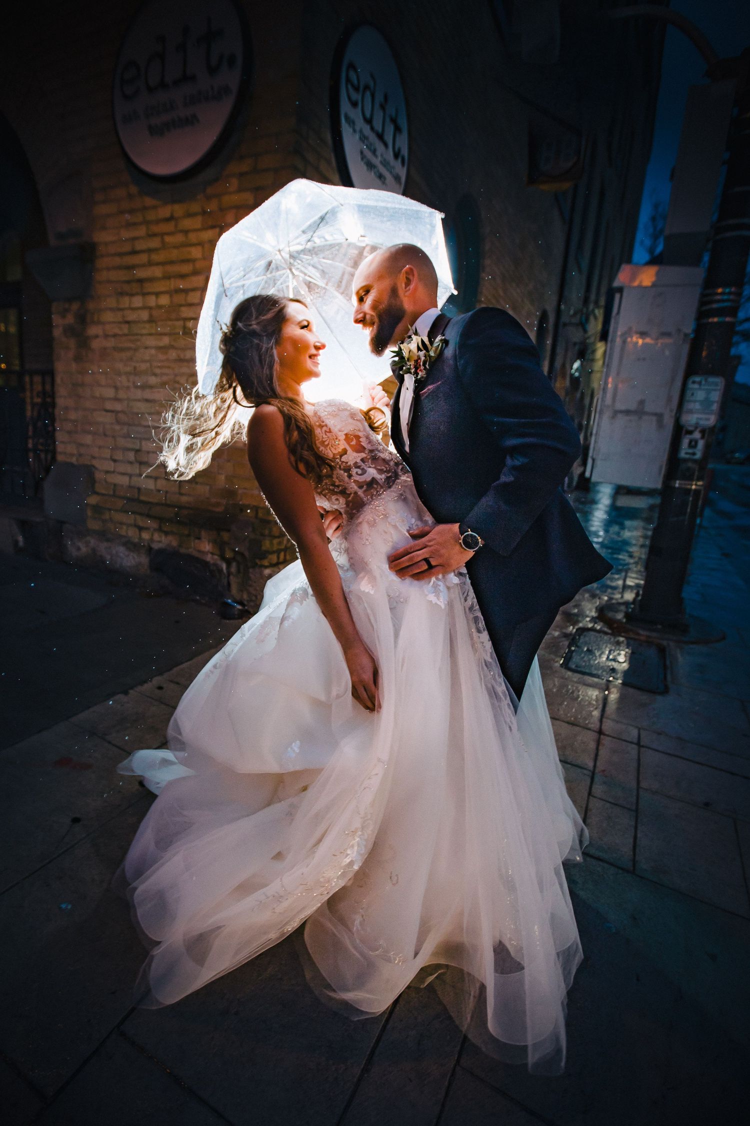 A dramatic wedding photo with a couple dancing against a brick wall backdrop at night.