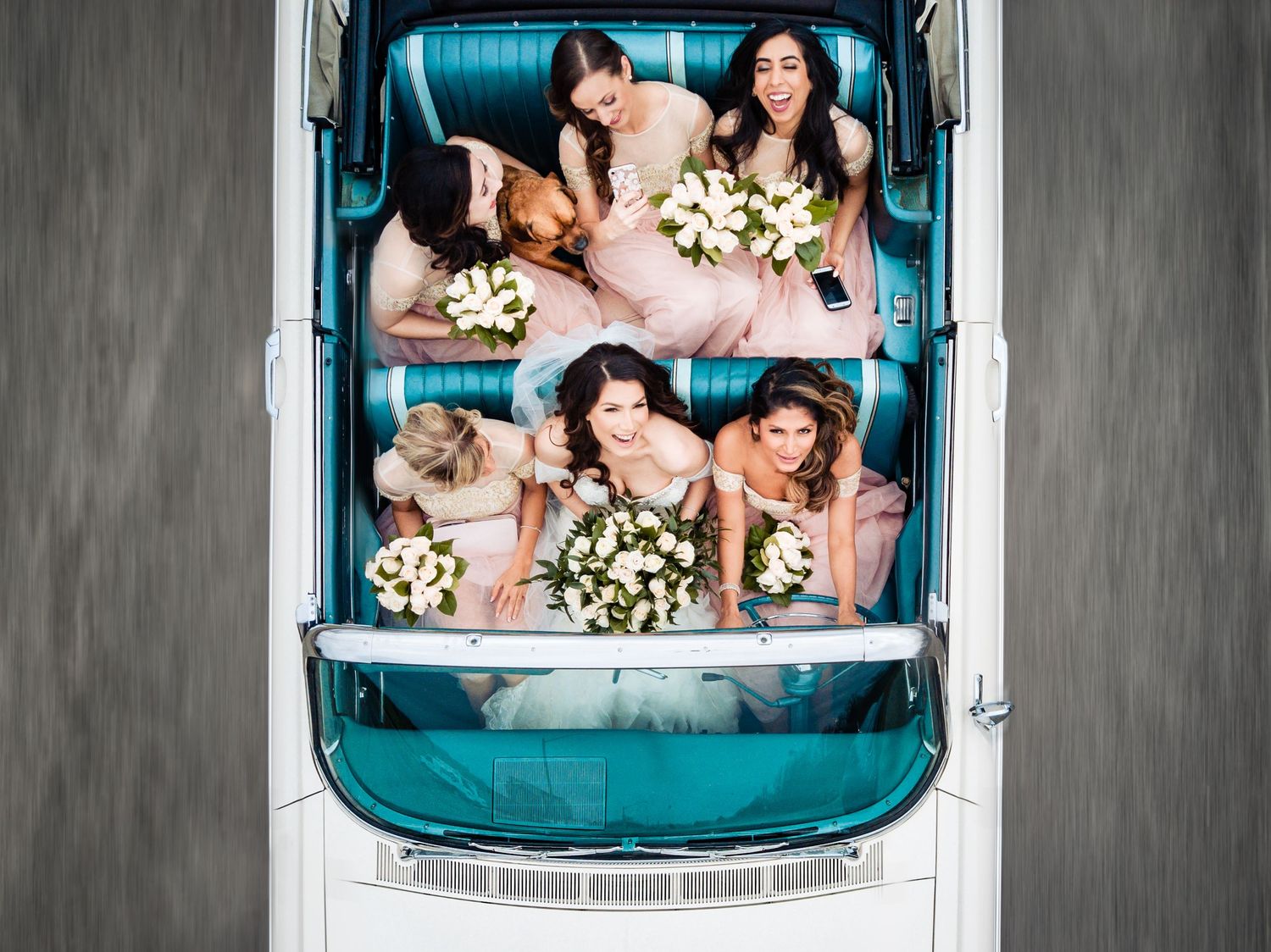 Wedding party poses in vintage turquoise convertible car for fun group photo.