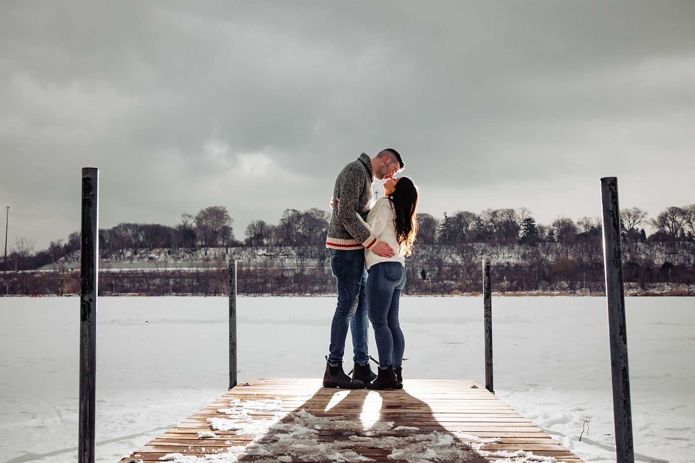 Romantic couple walking together on a snowy wooden dock by a frozen lake in winter.