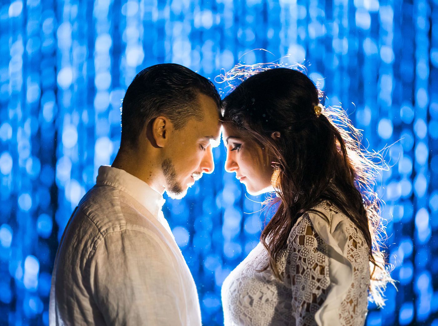 Couple dancing together against a blue bokeh light background creating a romantic atmosphere.