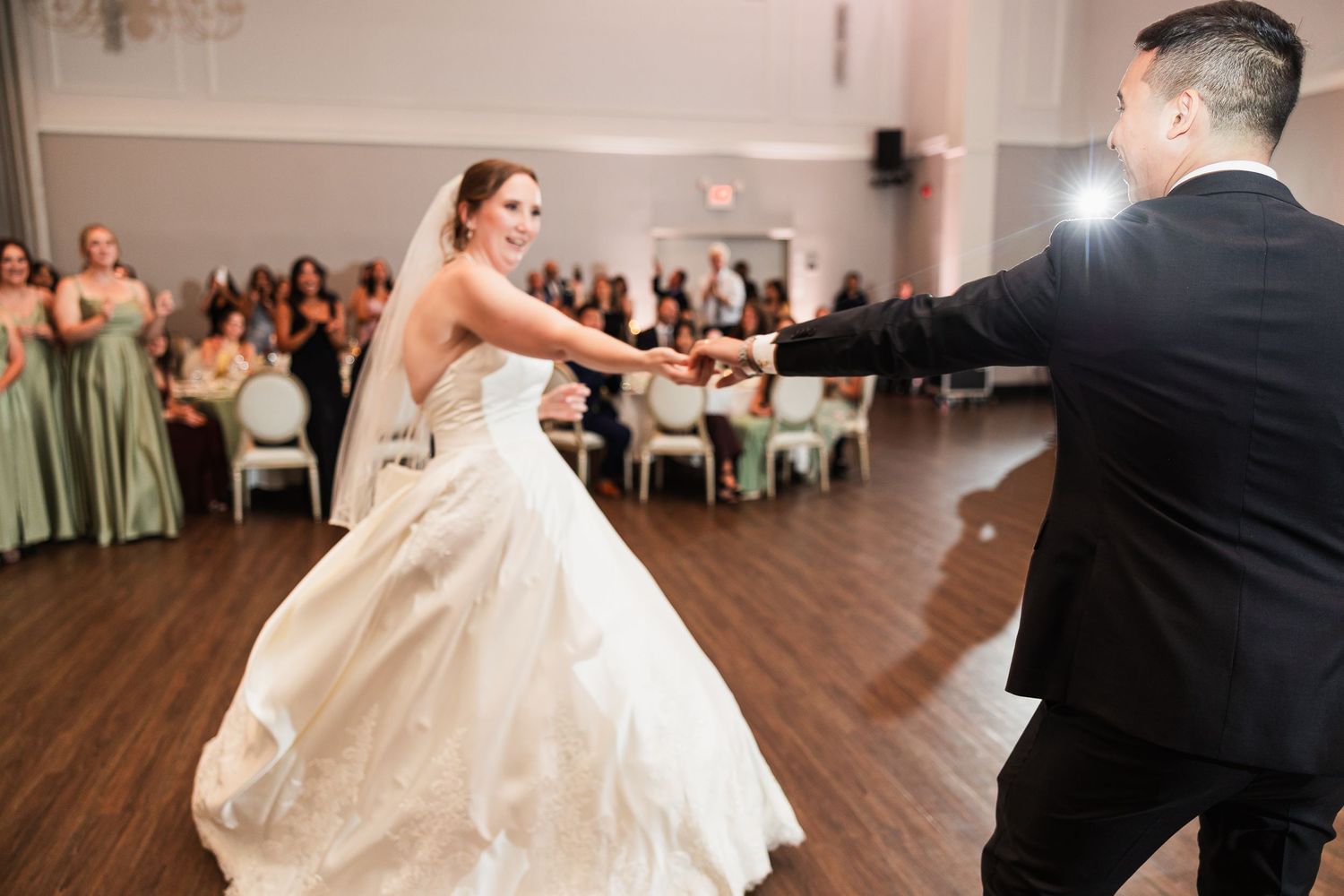 Bride and groom share their first dance at a wedding reception, with guests seated in the background.
