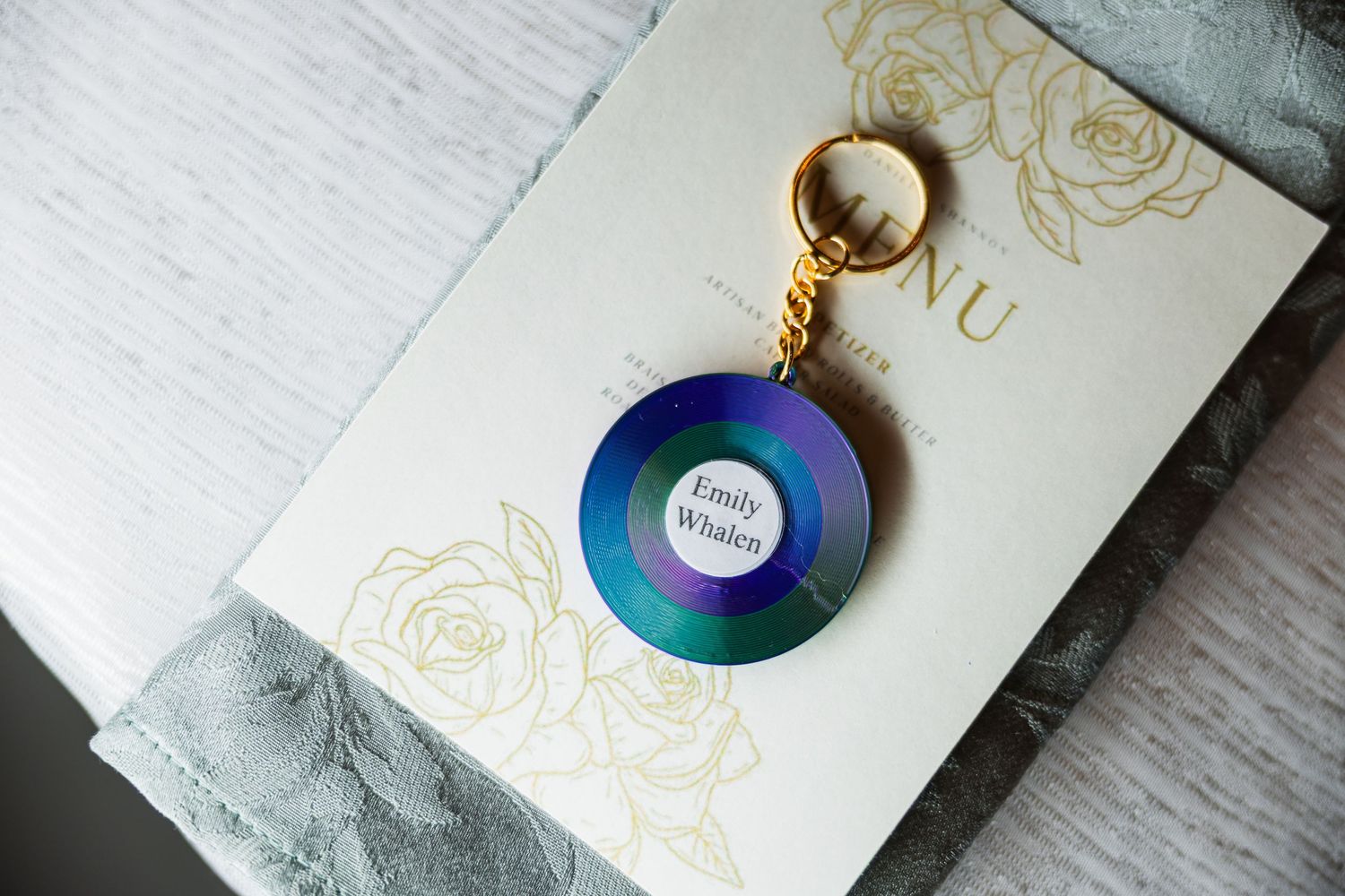Custom iridescent vinyl record keychain wedding favor with guest name on elegant invitation suite.