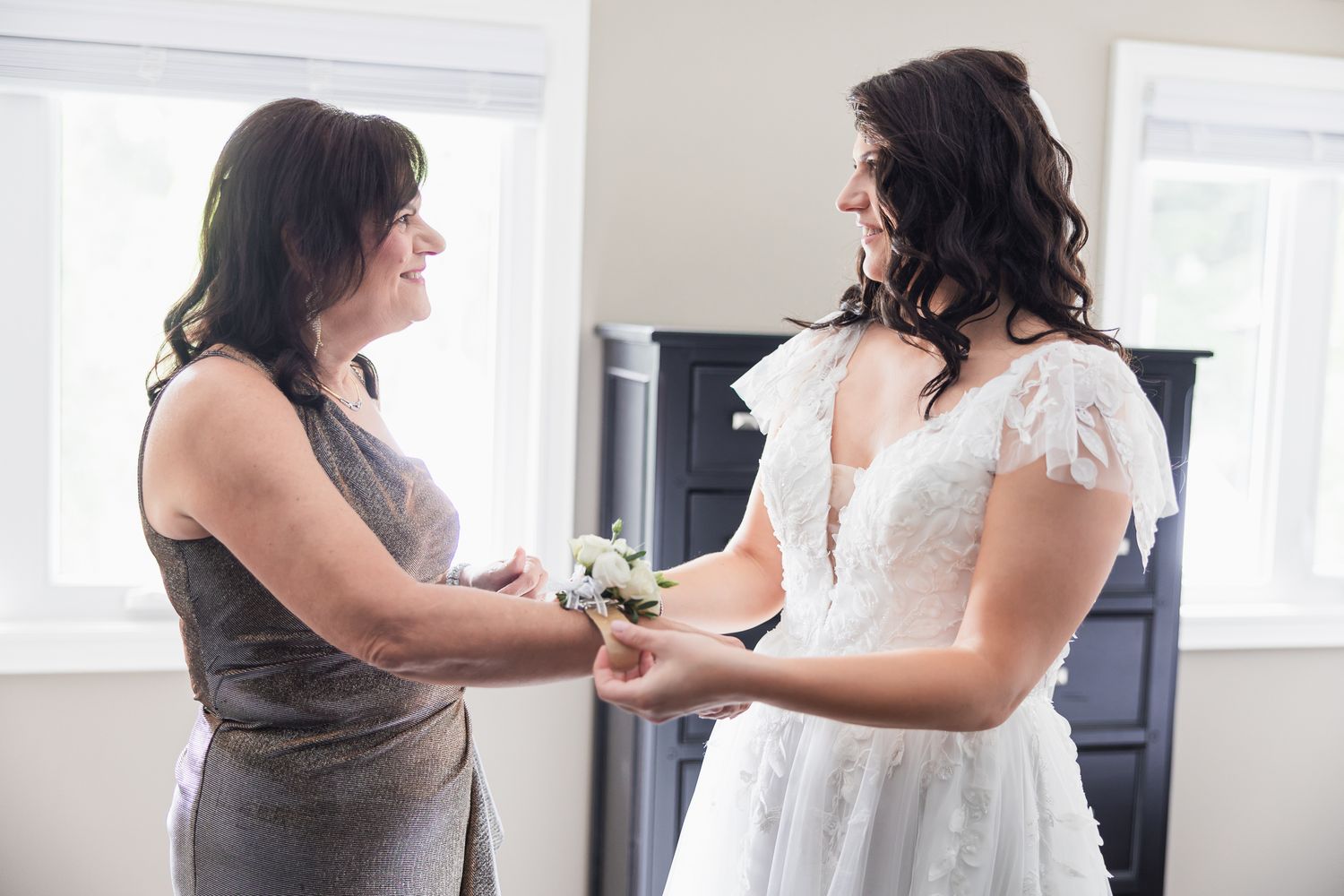 Bride in lace wedding dress holding bouquet with woman in gray dress before wedding.