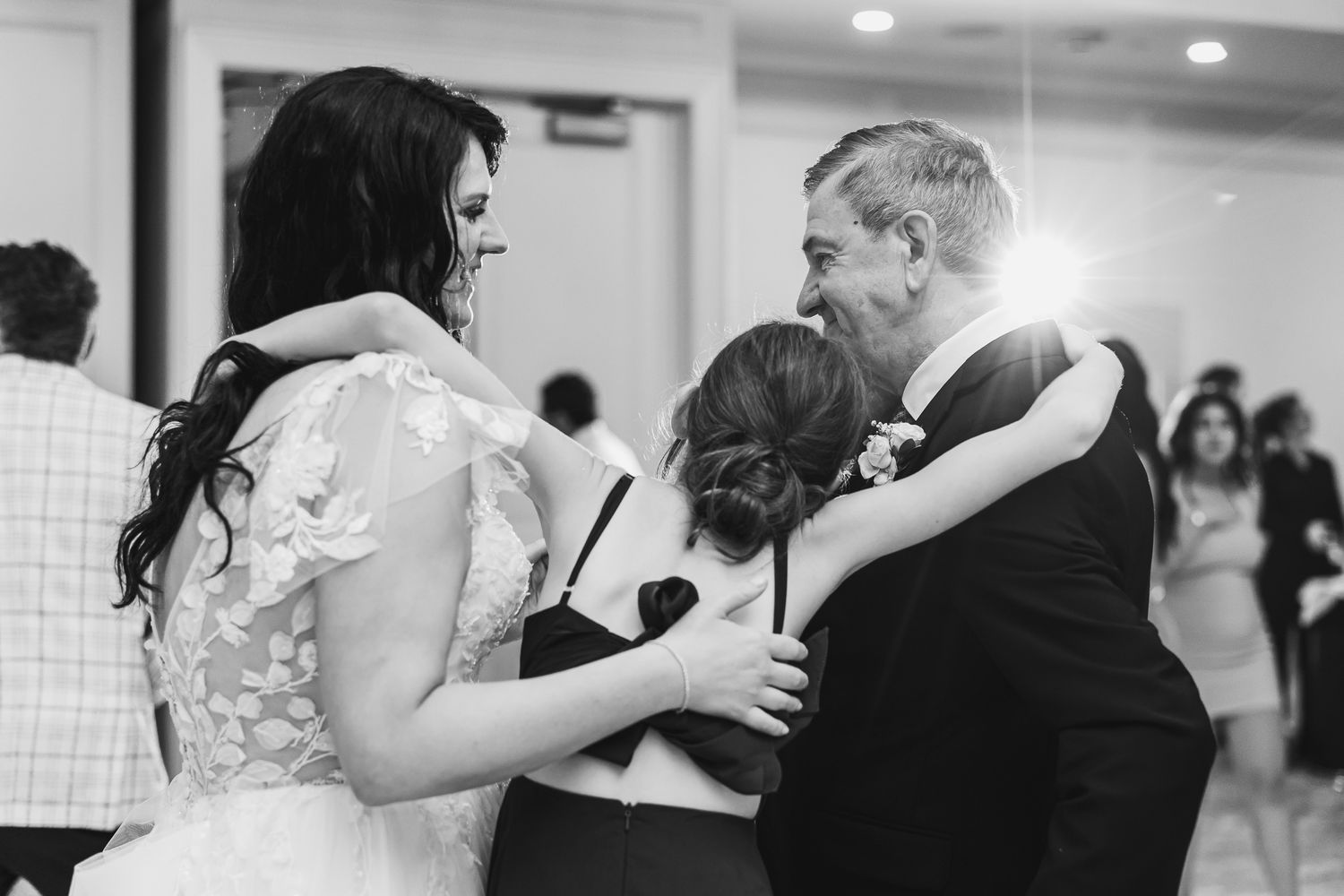 Black and white photo of a bride hugging guests at a wedding reception celebration.