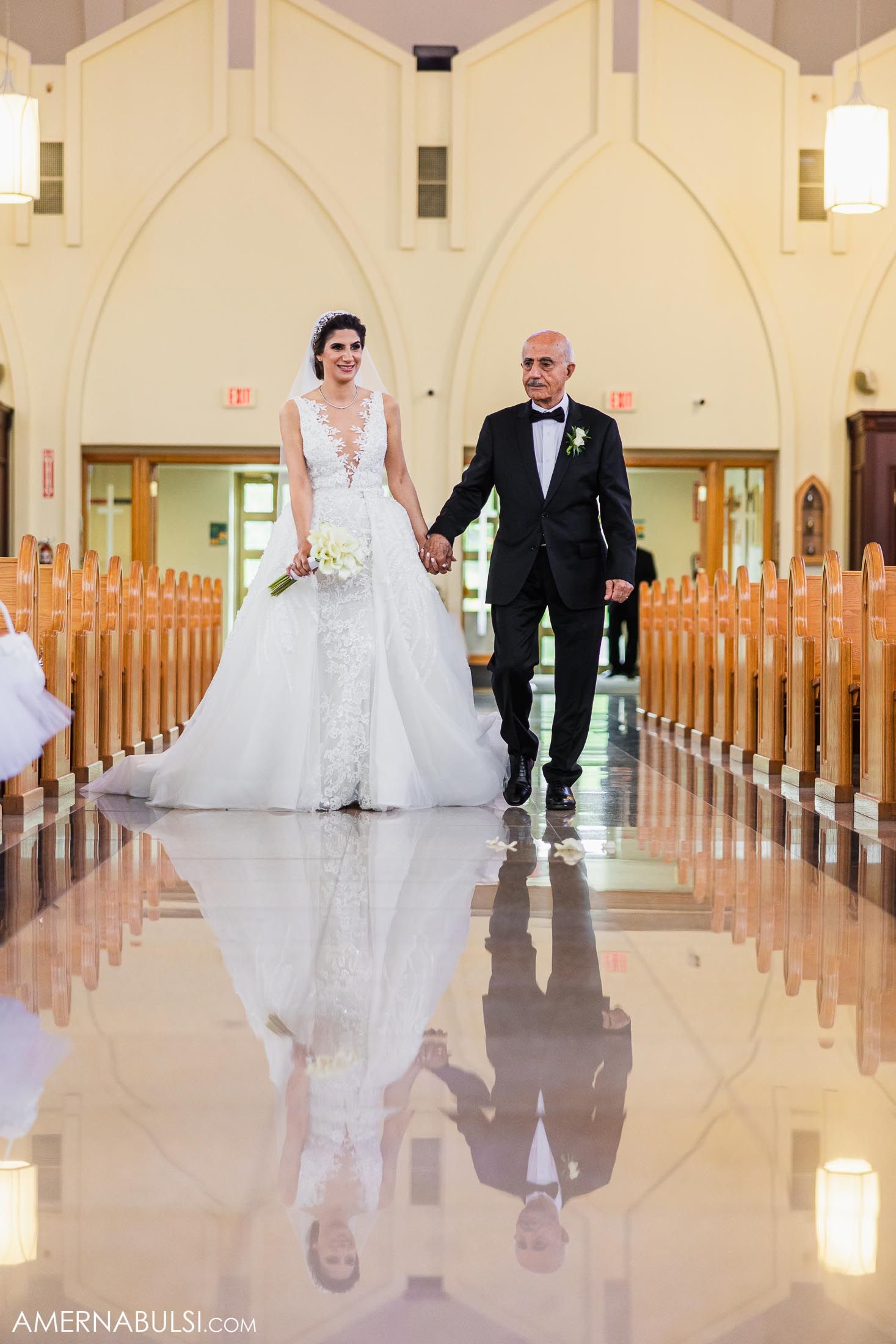 Newlywed couple walking down church aisle with their reflection showing in polished floor.