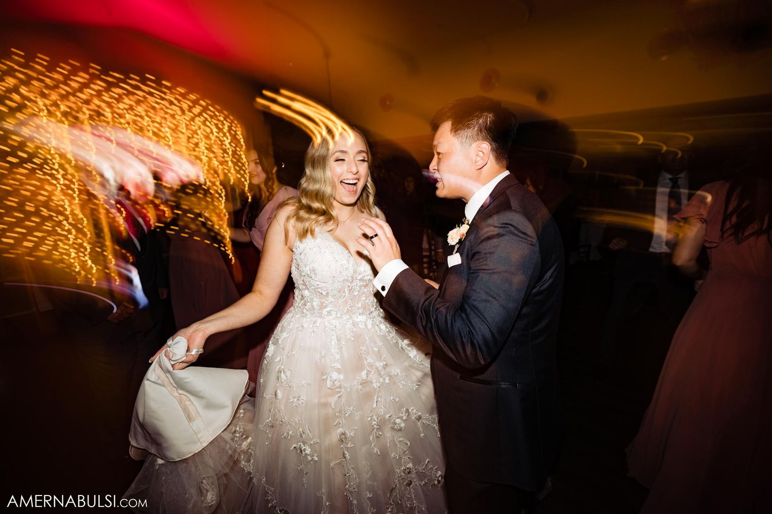A couple dances under warm lighting at their wedding reception.