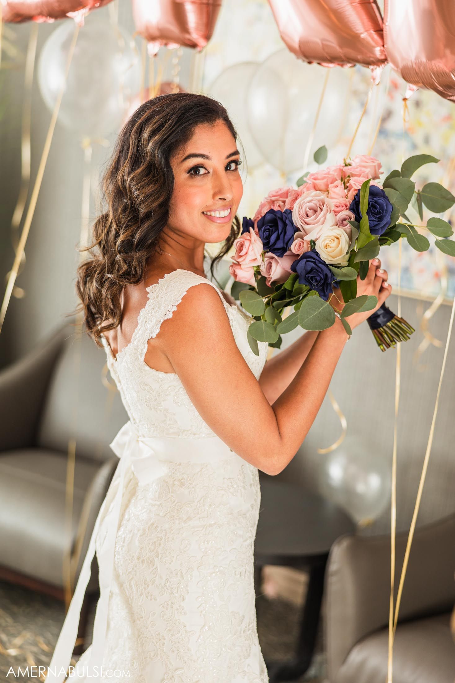 Bride holds pink and navy floral bouquet with rose gold balloons in background.