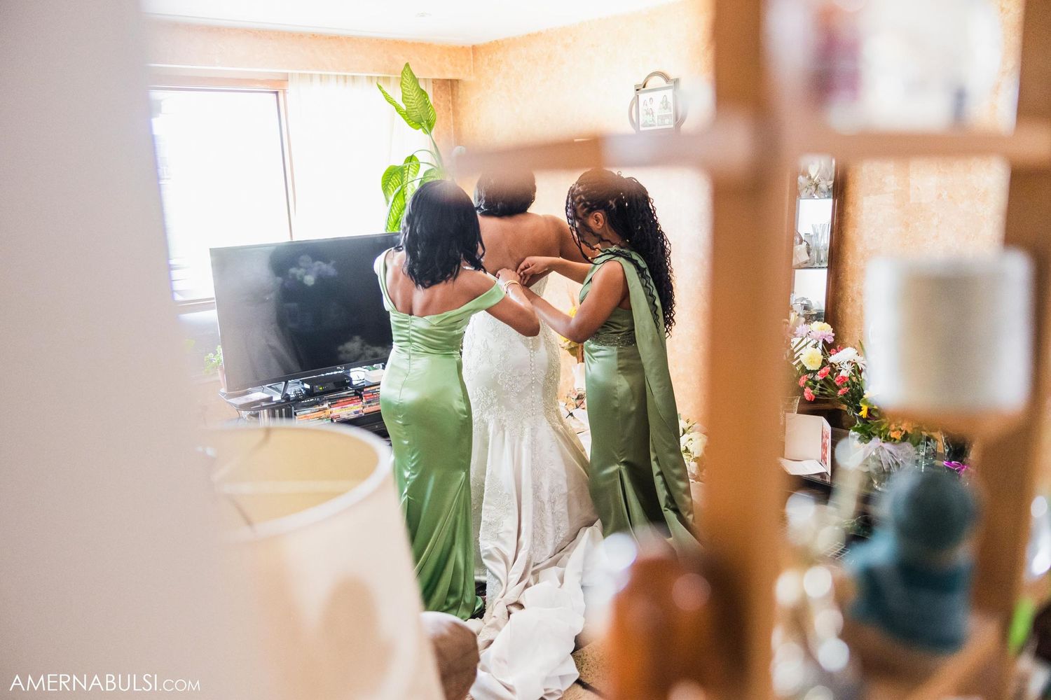Bridesmaids in sage green dresses help adjust a white wedding gown during pre-ceremony preparations.