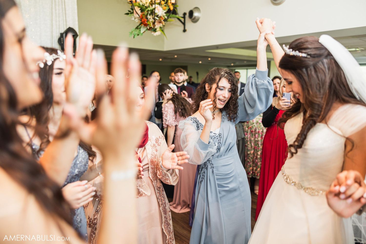 Wedding guests raise hands and dance together during reception celebration.