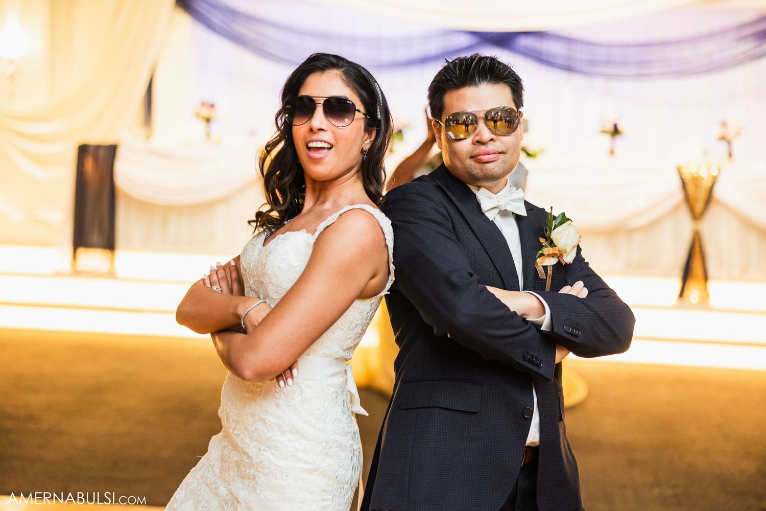 Stylish couple in wedding attire strike a cool pose wearing sunglasses indoors.