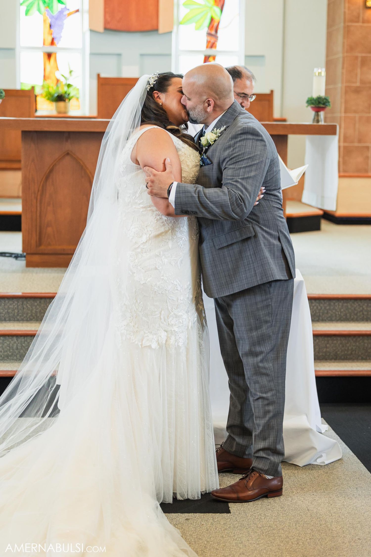 A couple shares their first kiss during their wedding ceremony in a church with palm tree decorations.