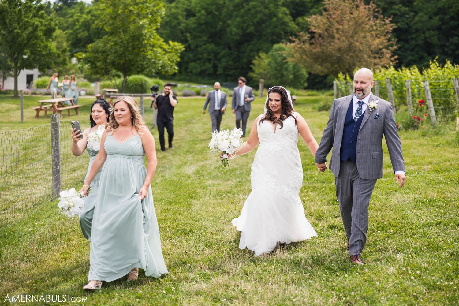 Wedding party walking through vineyard grounds in formal attire.